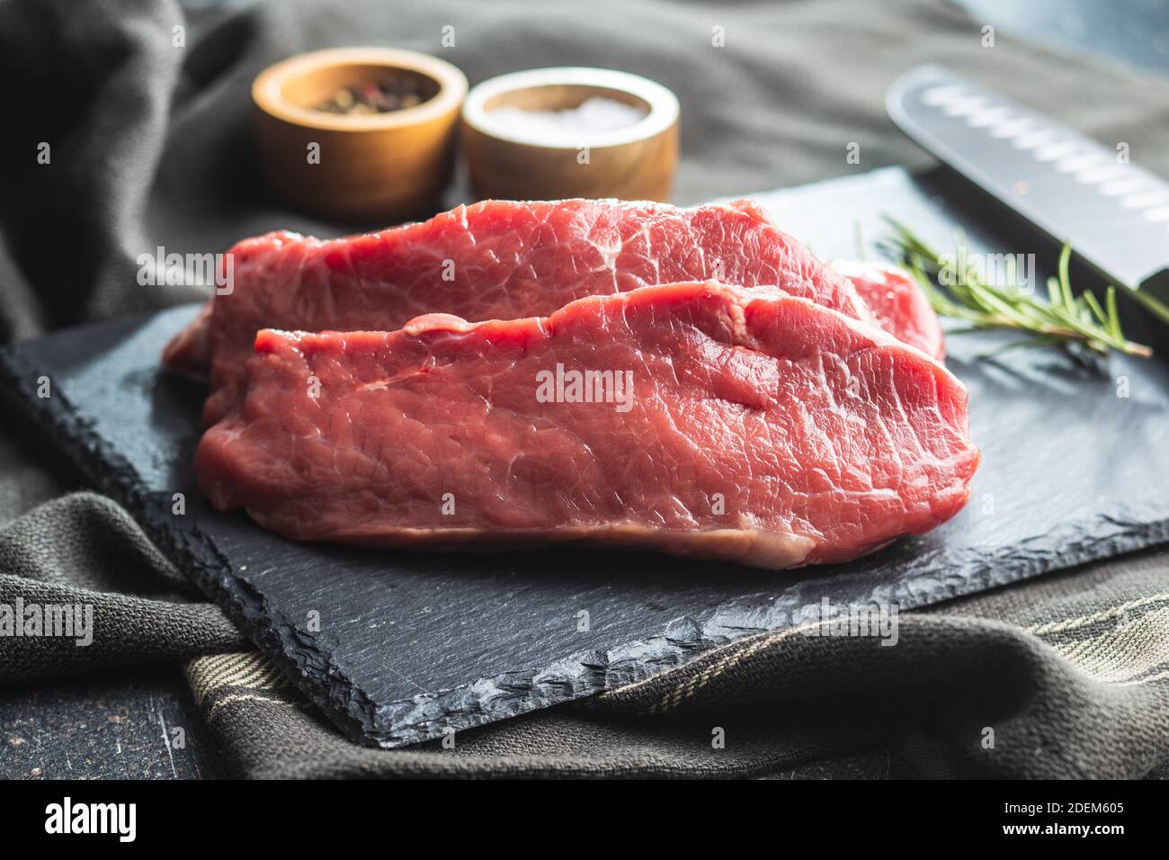 Tranche le steak de striploine brut sur une planche à découper en pierre noire. Banque D'Images