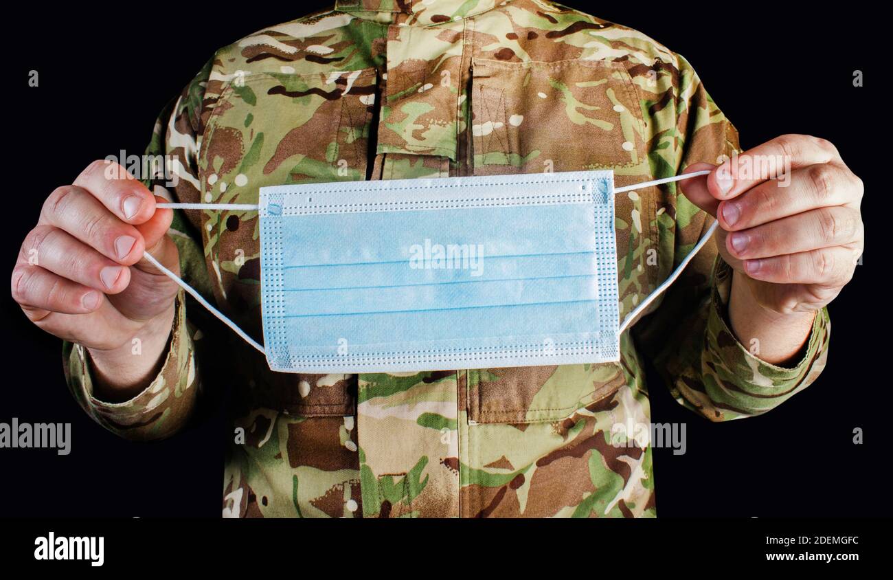 Photo d'un militaire en uniforme camouflé portant un masque médical de protection sur fond noir. Banque D'Images