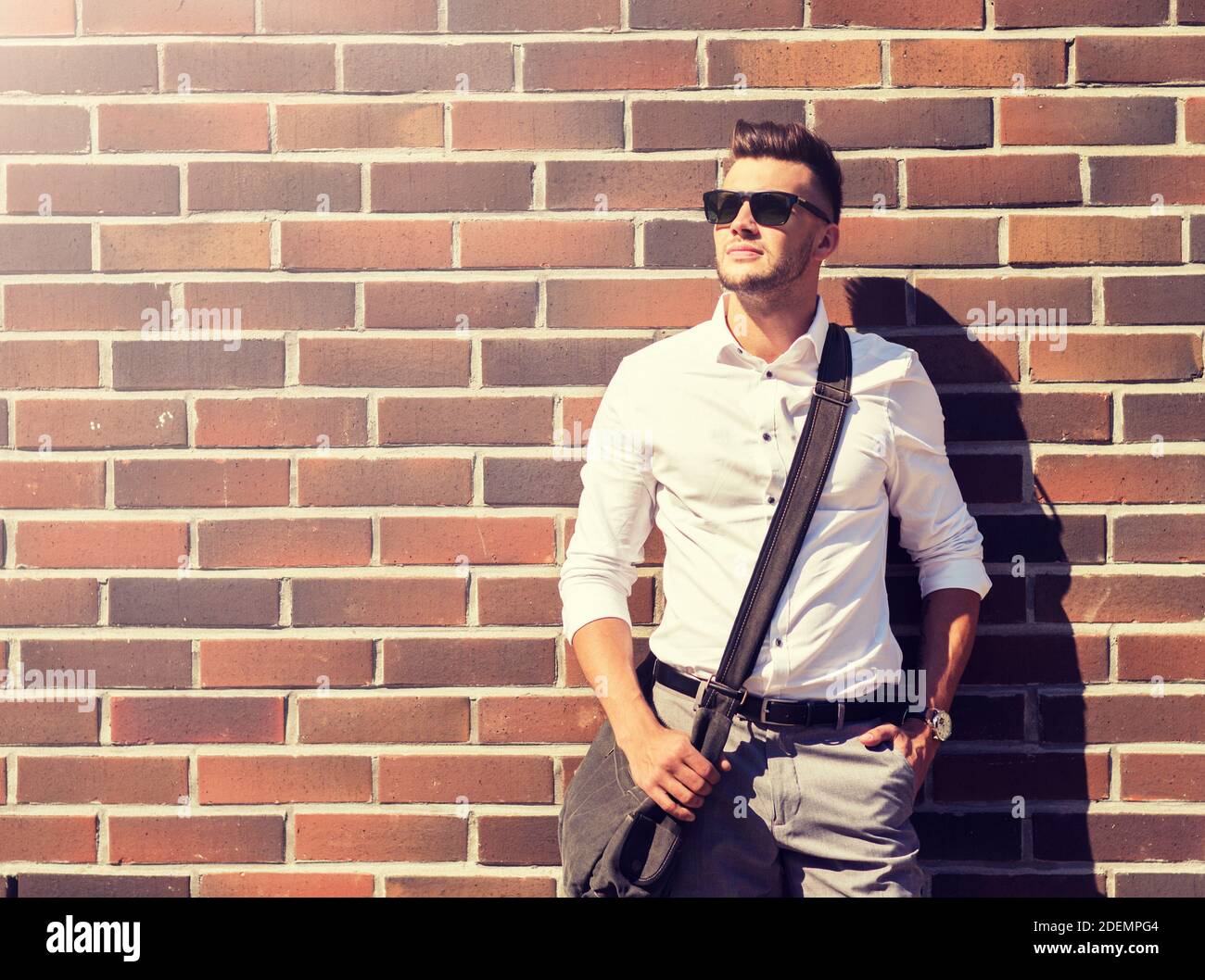 Jeune homme à lunettes avec sac sur brickwall Banque D'Images