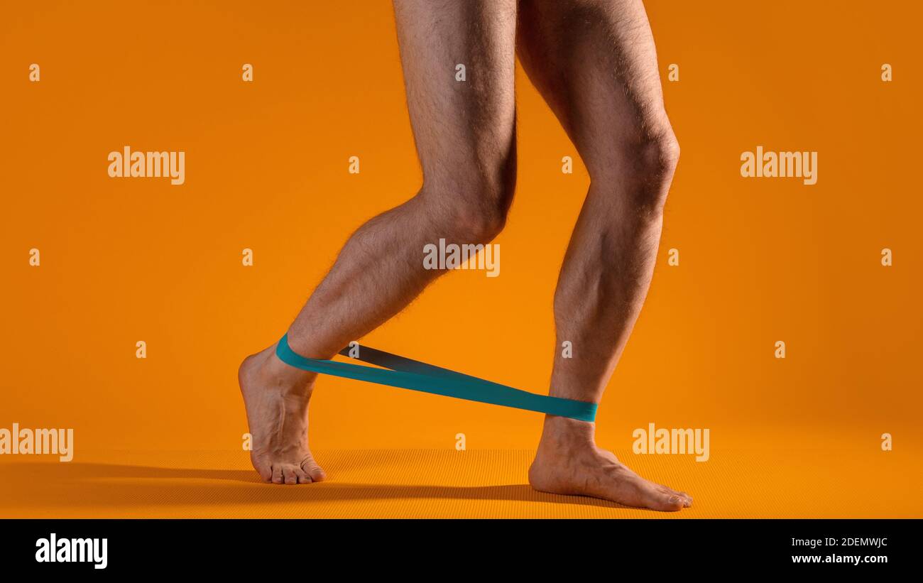 Musclés hommes jambes avec élastique bande pour la forme physique, faire des exercices pour tendre les muscles de la jambe. Parties du corps, fond jaune. Banque D'Images