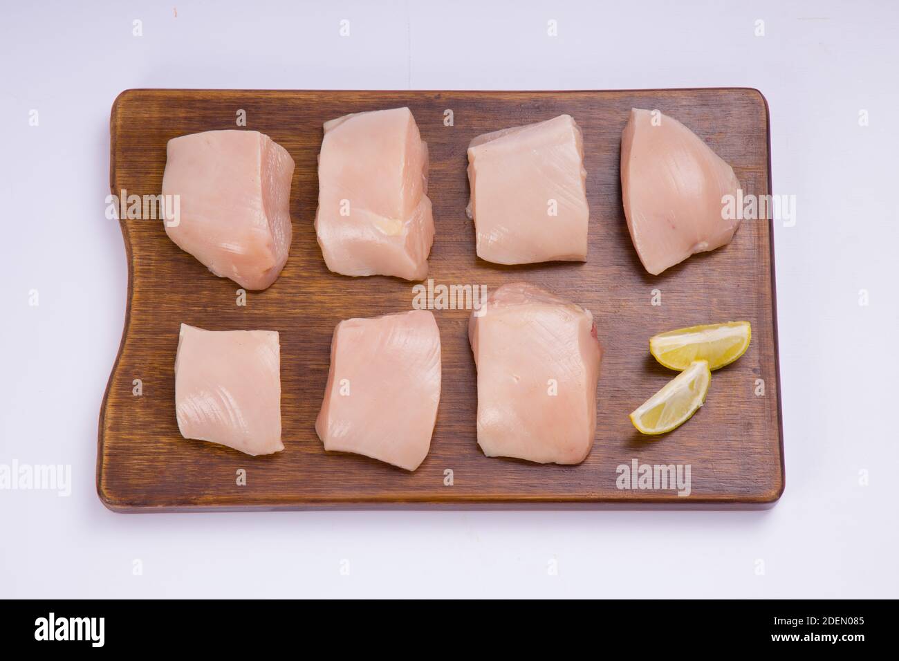 Poulet cru tendre frites coupées sans peau sur bois planche et garniture de tranches de citron sur fond blanc Banque D'Images