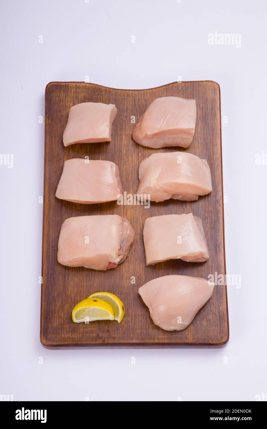 Poulet cru tendre frites coupées sans peau sur bois planche et garniture de tranches de citron sur fond blanc Banque D'Images