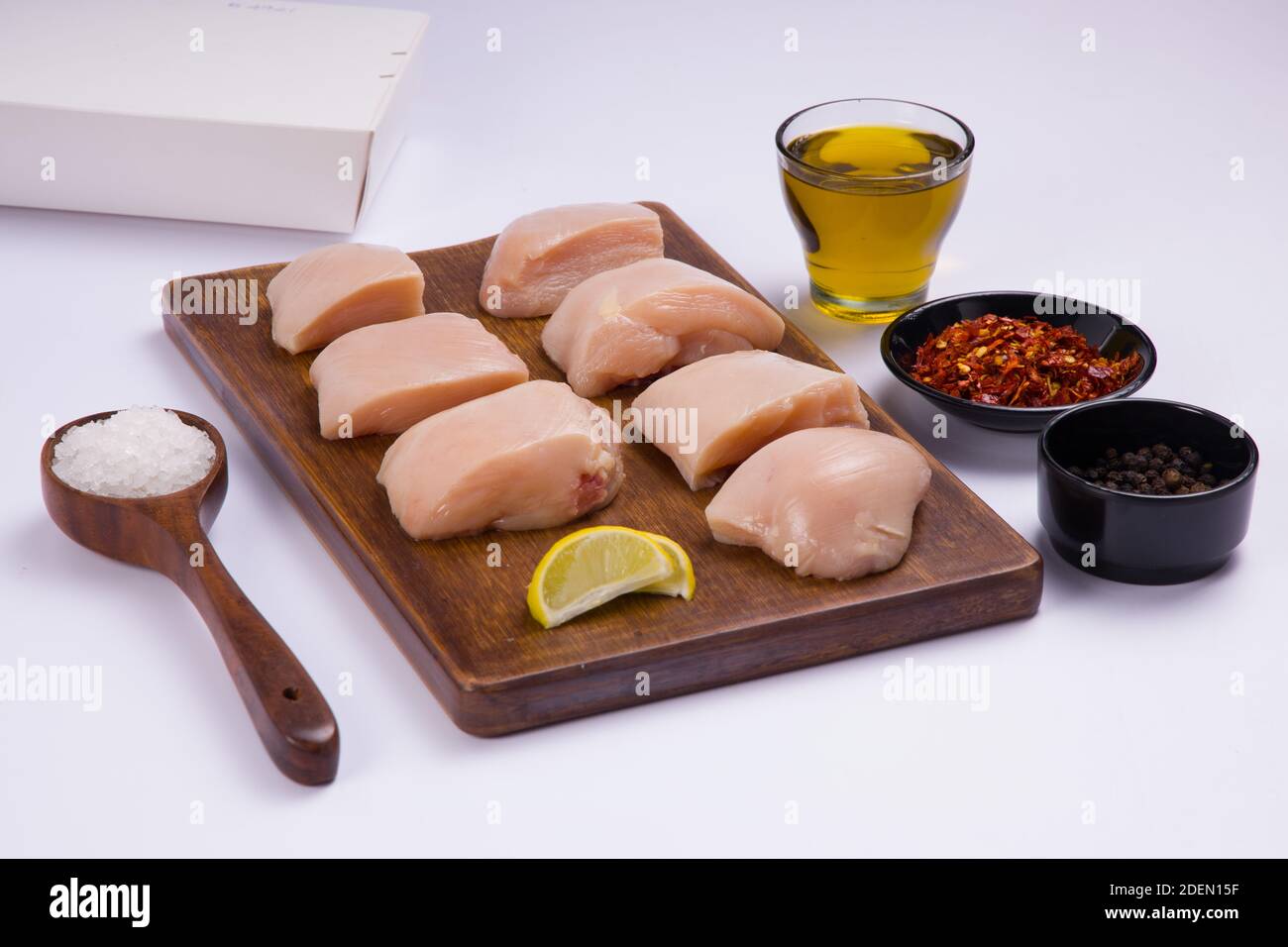 Poulet cru tendre friture coupée sans peau sur bois et garni d'huile, de tranches de citron, de flocons de piment et de poivre noir de couleur blanche Banque D'Images