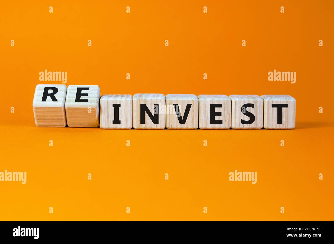 Symbole de réinvestissement. Cubes en bois inversés avec les mots « investir - réinvestir ». Magnifique arrière-plan orange. Concept d'entreprise et de réinvestissement. Copier l'espace. Banque D'Images