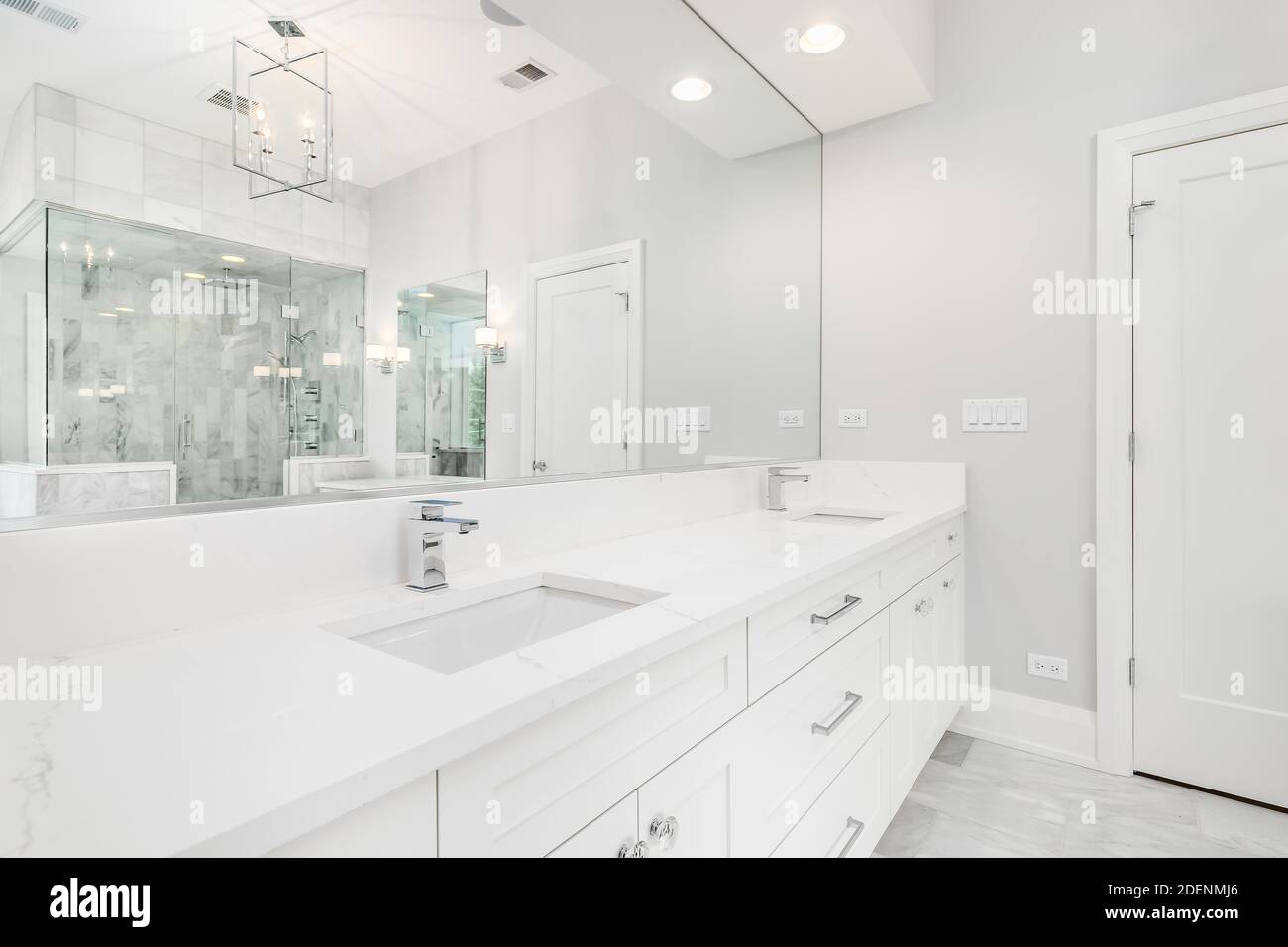 Une grande salle de bains luxueuse avec baignoire îlot, meuble-lavabo blanc et douche en verre avec carrelage en marbre et banquette. Banque D'Images