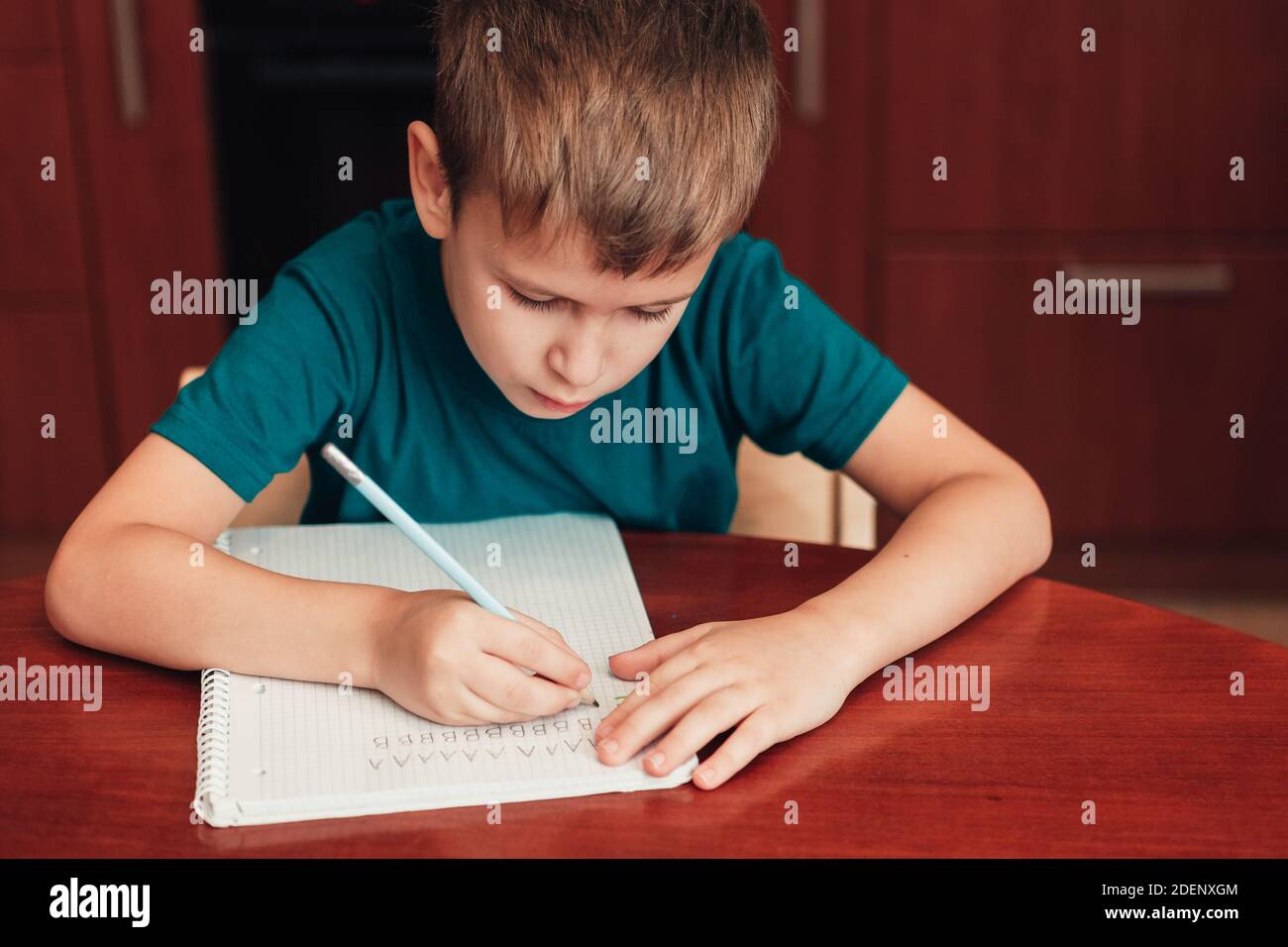 un enfant de 7 ans écrit des lettres dans un carnet assis près de table dans la cuisine Banque D'Images