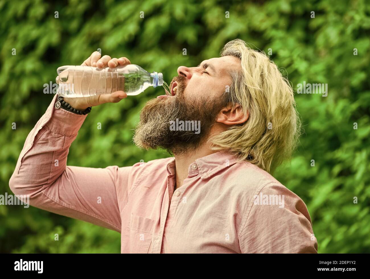 Chaleur estivale. Boire de l'eau claire. Équilibre de l'eau. Homme barbu touriste eau bouteille plastique nature fond. Un gars assoiffé boit des bouteilles Banque D'Images