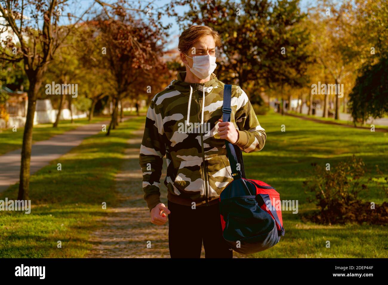 Jeune homme qui va à la salle de gym avec son sac sur son épaule. Porter un masque de protection est la randonnée à travers les bois. Banque D'Images