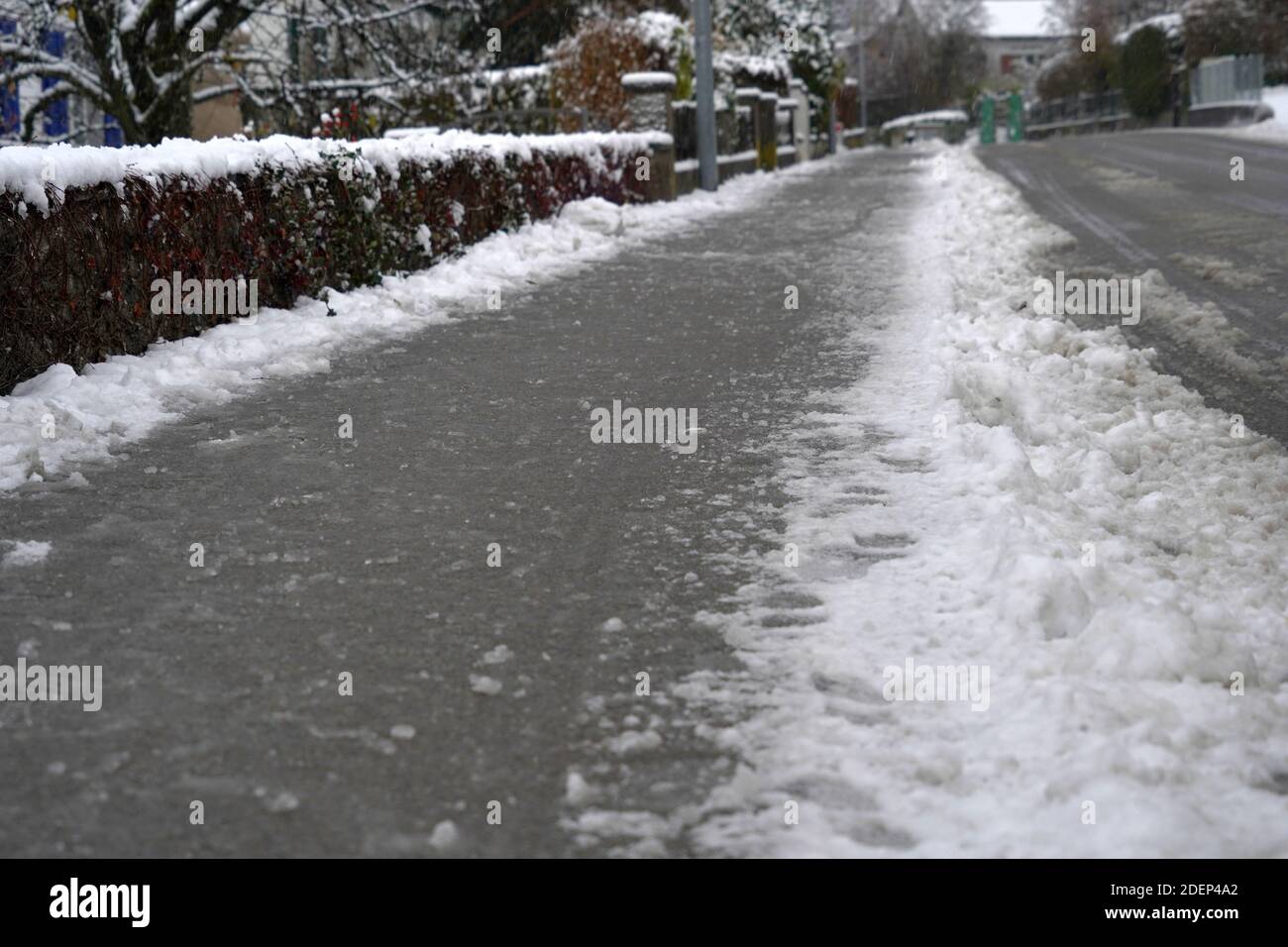 Trottoir et rue d'un village en Suisse en hiver. La neige est traitée avec du sel de voirie pour rendre la rue moins glissante et garantir la sécurité. Banque D'Images
