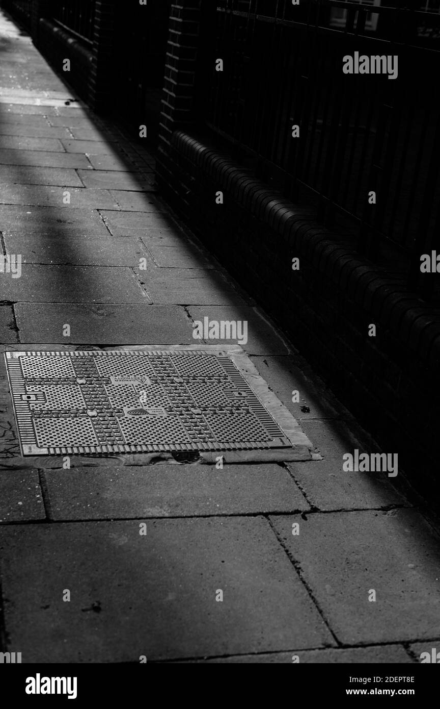 Image monochrome noir et blanc en regardant sur une chaussée avec de longues ombres sur une couverture de trou d'homme Banque D'Images