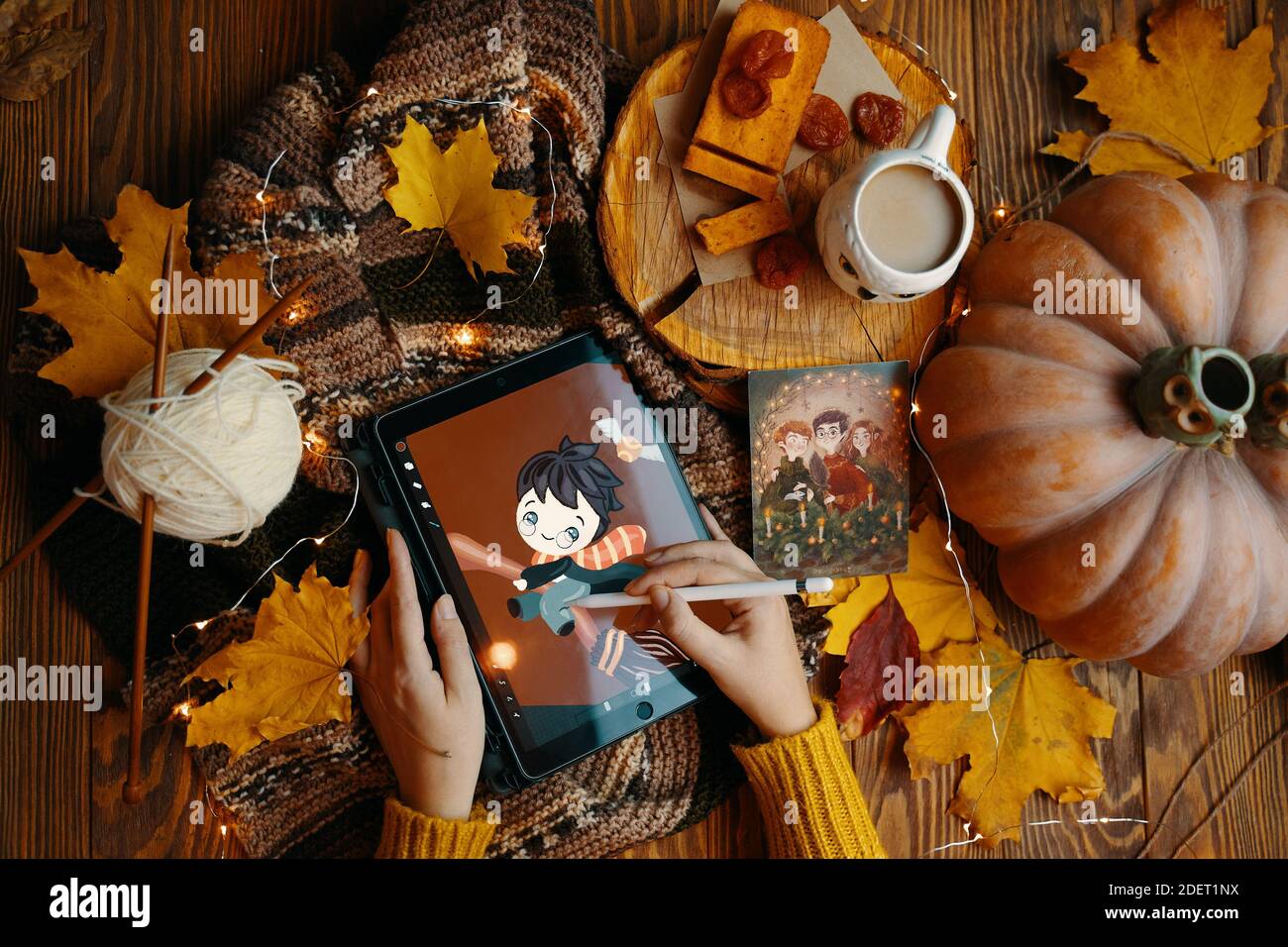 Jeune femme dans un chandail tire sur un iPad Pro Harry Potter joue Quidditch sur un bâton de couvée. Foulard, café, tarte, citrouille, feuilles et guirlande sur une table en bois. Bichkek, Kirghizistan - 1er novembre 2019. Banque D'Images