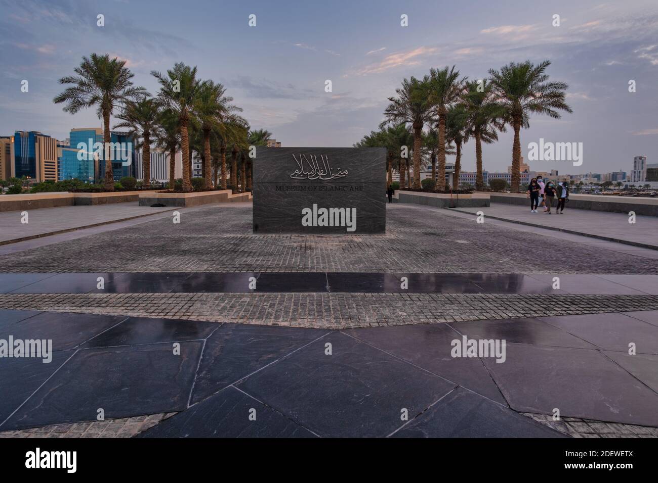 Panneau du musée d'art islamique à Doha, Qatar, devant l'entrée principale du musée avec palmiers, personnes marchant et horizon de Doha en arrière-plan Banque D'Images