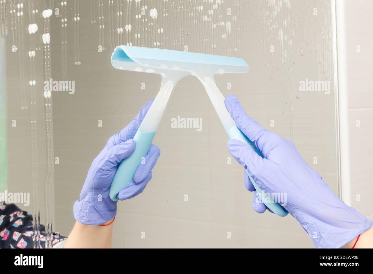 main femelle dans un gant en caoutchouc bleu essuie-tout a miroir dans la salle de bains sur fond de carreaux blancs Banque D'Images