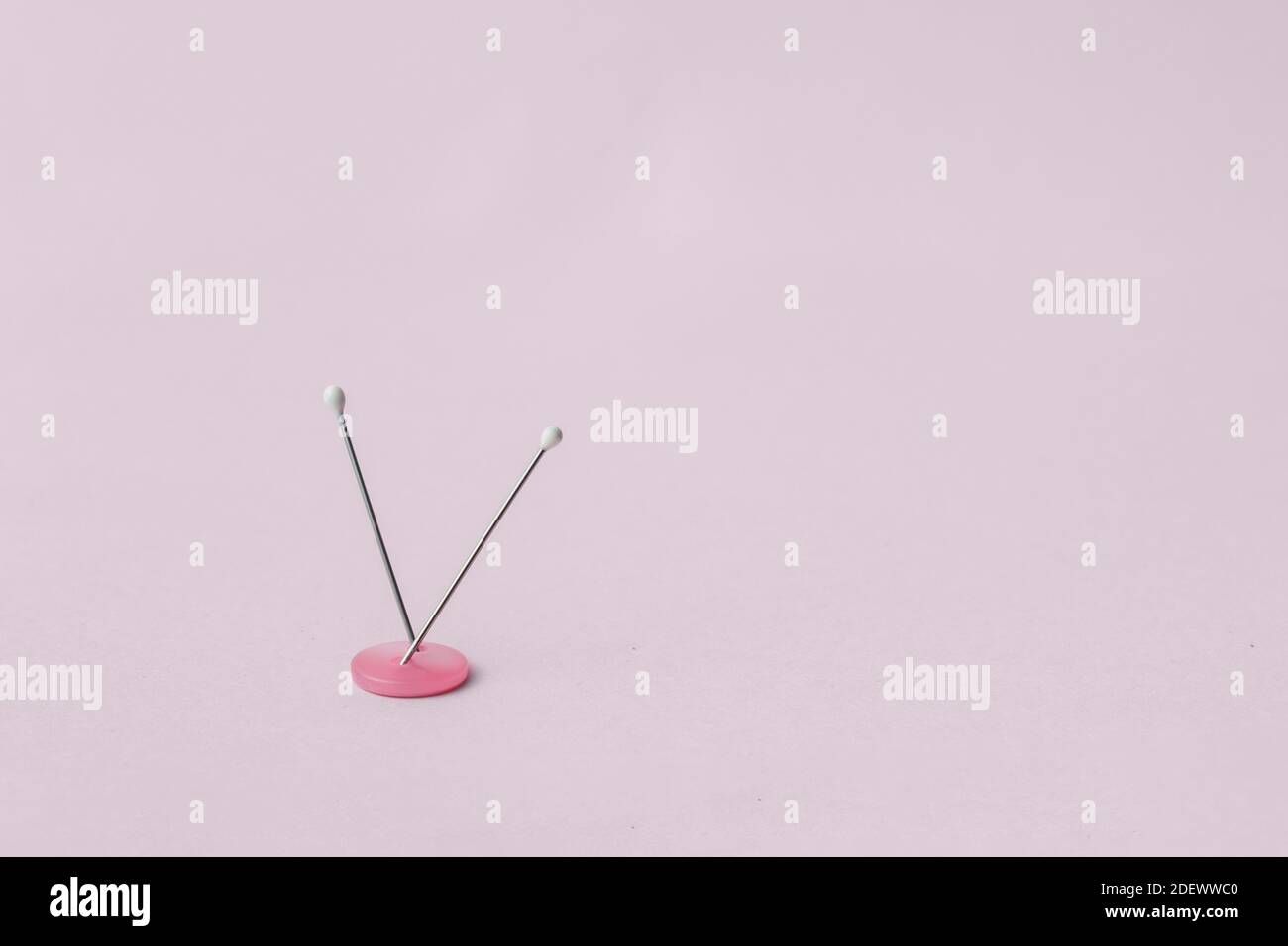 Deux aiguilles à tête perlée coincées dans un bouton à deux trous sur fond rose. Banque D'Images