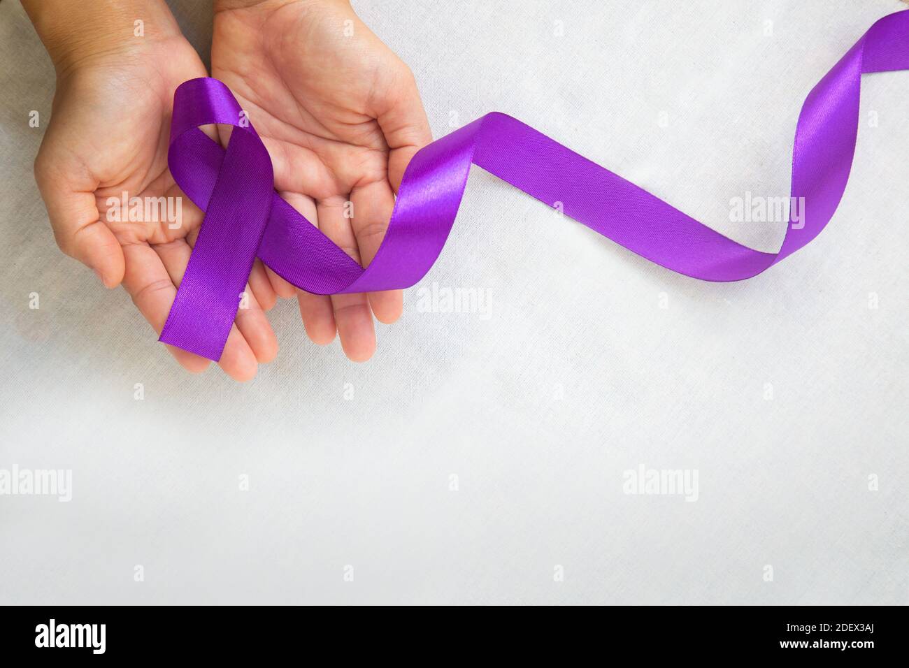 Mains tenant ruban violet ou violet sur tissu blanc avec espace de copie. Cancer du pancréas, sensibilisation au cancer du testicule, survivant du cancer, léiomyosarcome Banque D'Images