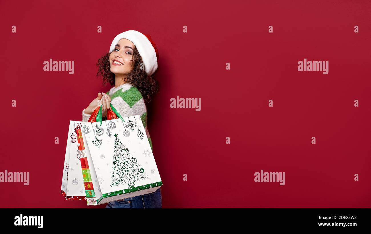 Belles femmes portant des sacs de Noël colorés sur fond rouge. Shopping de Noël et Bonne Année. Banque D'Images