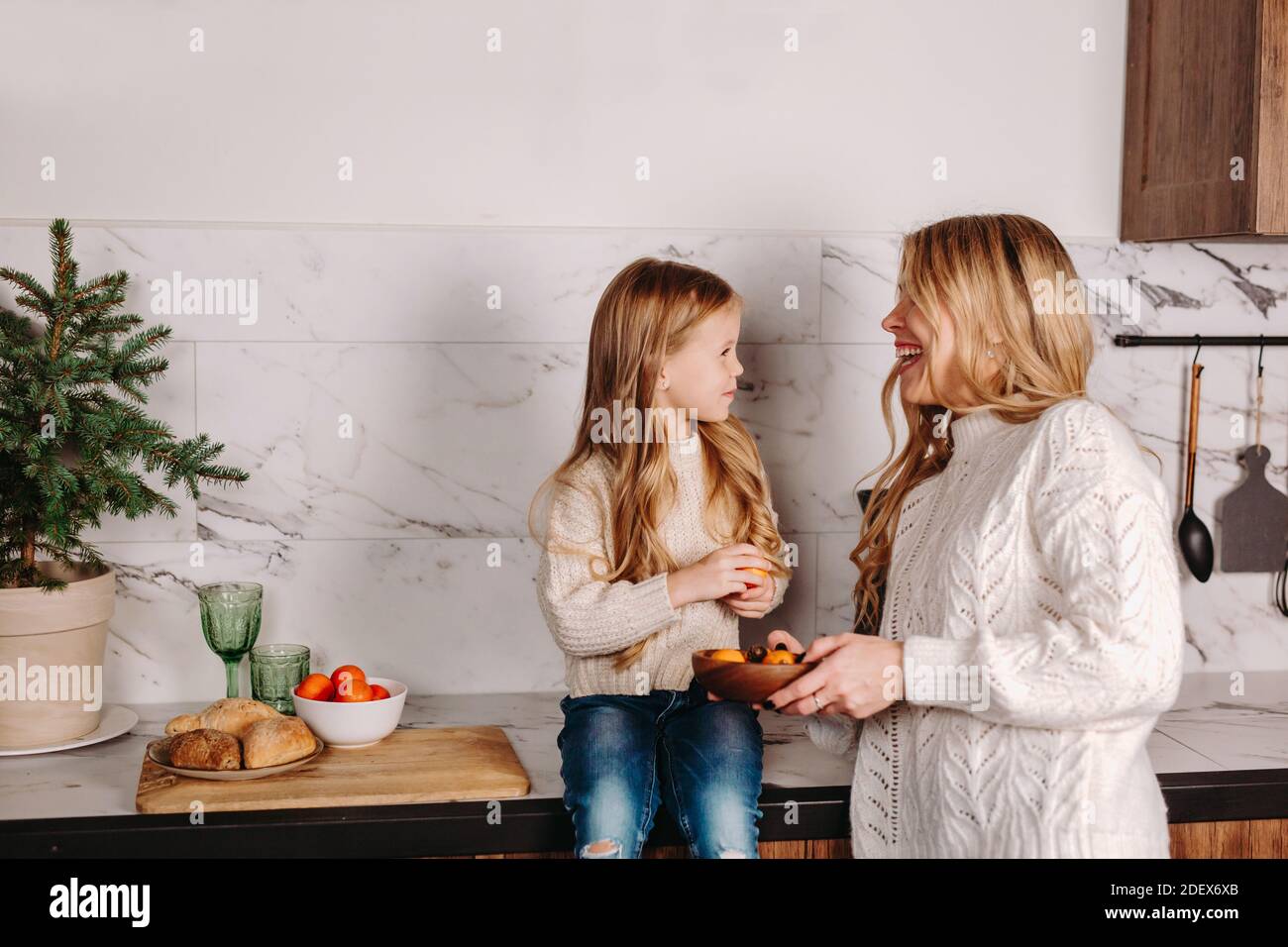 Mère heureuse avec fille mangeant des mandarins dans la cuisine Banque D'Images