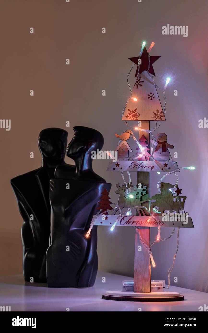 Petit sapin de Noël en bois décoré avec le Père Noël et un bonhomme de neige, illuminé de lumières colorées et de la sculpture d'un couple amoureux Banque D'Images