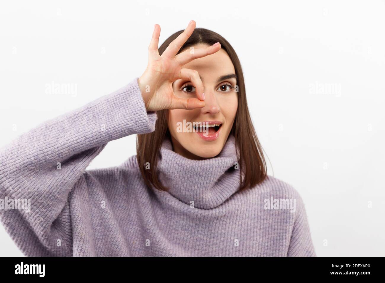 Gros plan de la jeune femme positive avec de longs cheveux regardant l'appareil photo par ok-geste, belle brune femelle avec les yeux sombres a amusant bon Banque D'Images