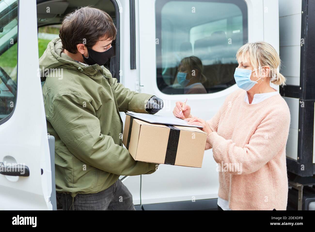 Le client ayant un masque facial donne la signature du service de livraison de colis pour livraison de colis dans la rue Banque D'Images