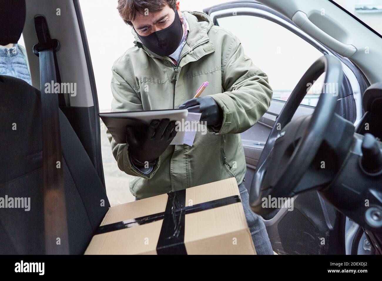 Personne chargée de la livraison de colis avec colis et liste de contrôle sur la voiture Avec masque facial en raison de Covid-19 Banque D'Images