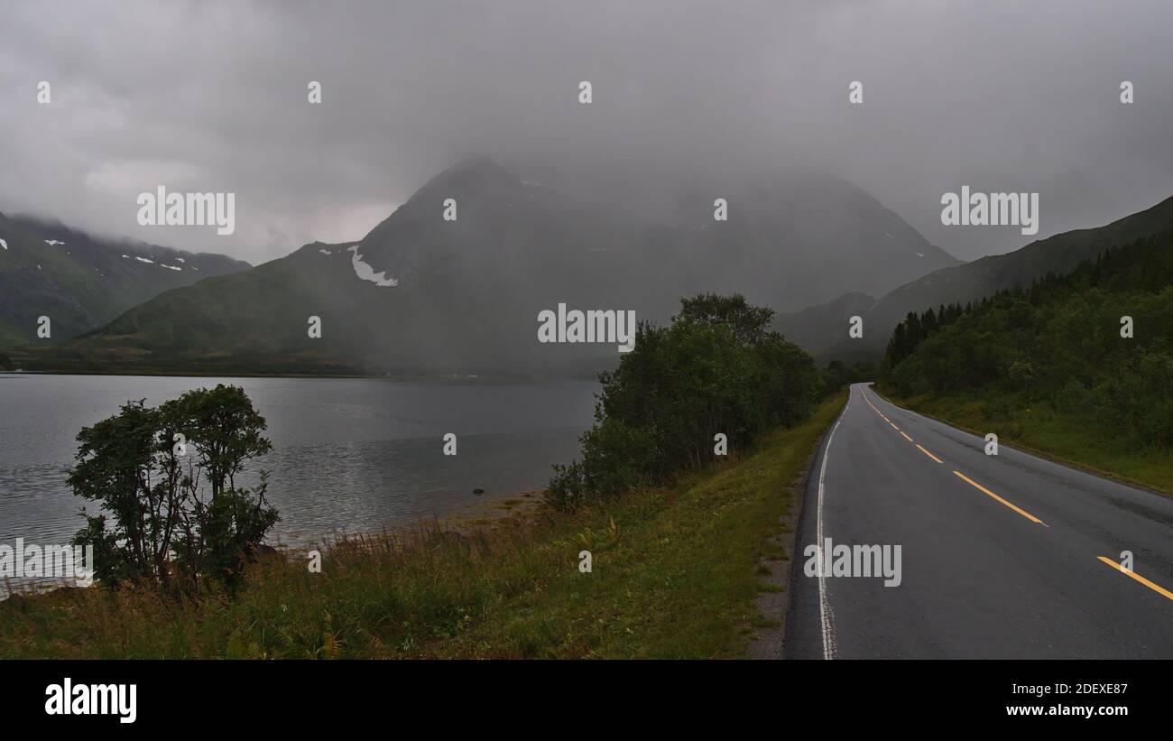 Vue sur la route de campagne pavée vide 85 à Gullesfjord, Hinnøya, Vesterålen dans le nord de la Norvège, le jour des pluies avec végétation verte, fjord et montagnes. Banque D'Images