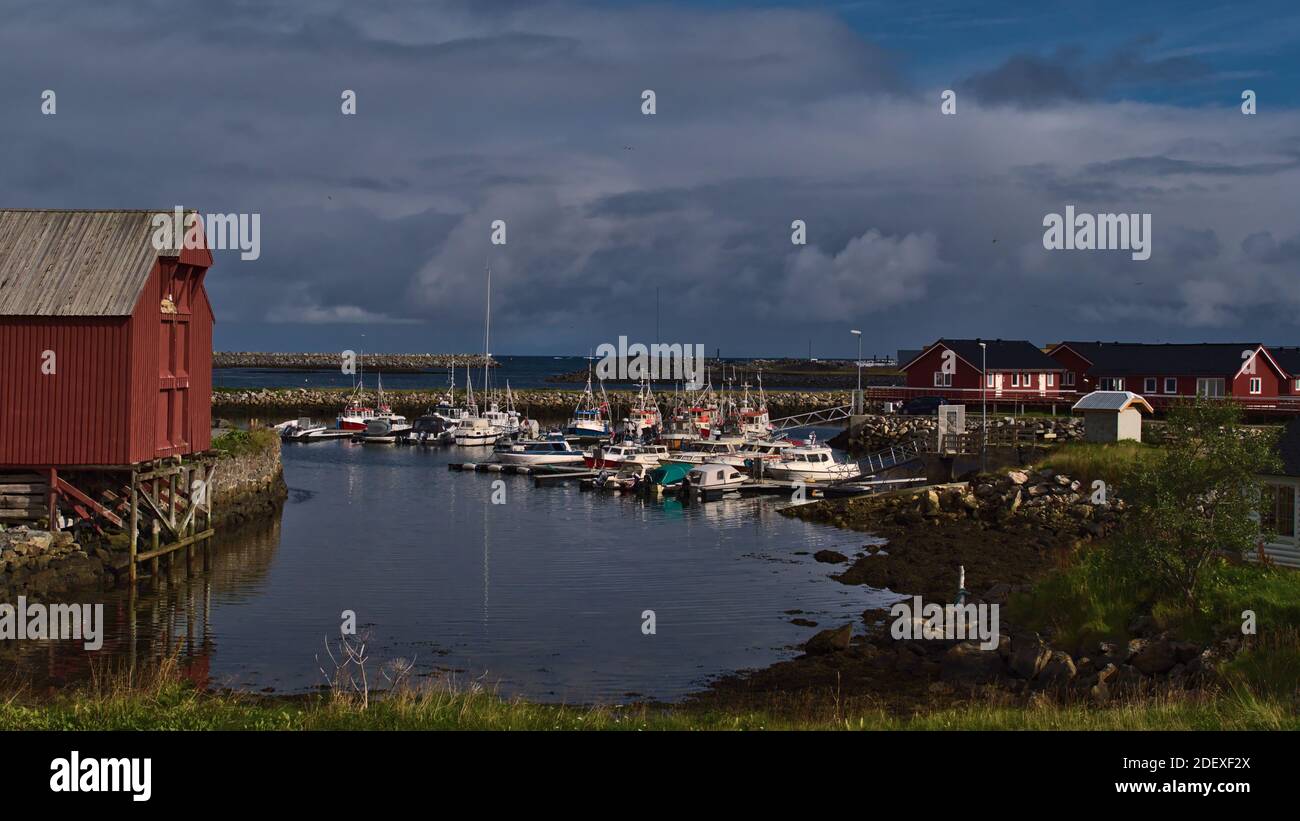 Vue sur le port du village de pêcheurs d'Andenes dans le nord de l'île d'Andøya, Vesterålen, Norvège avec bateaux d'amarrage, brise-lames et maisons rouges typiques. Banque D'Images