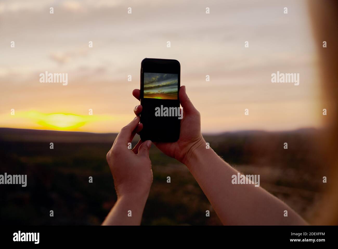 Gros plan des mains d'une jeune femme tenant un appareil mobile pour prendre des photos du lever du soleil le matin Banque D'Images