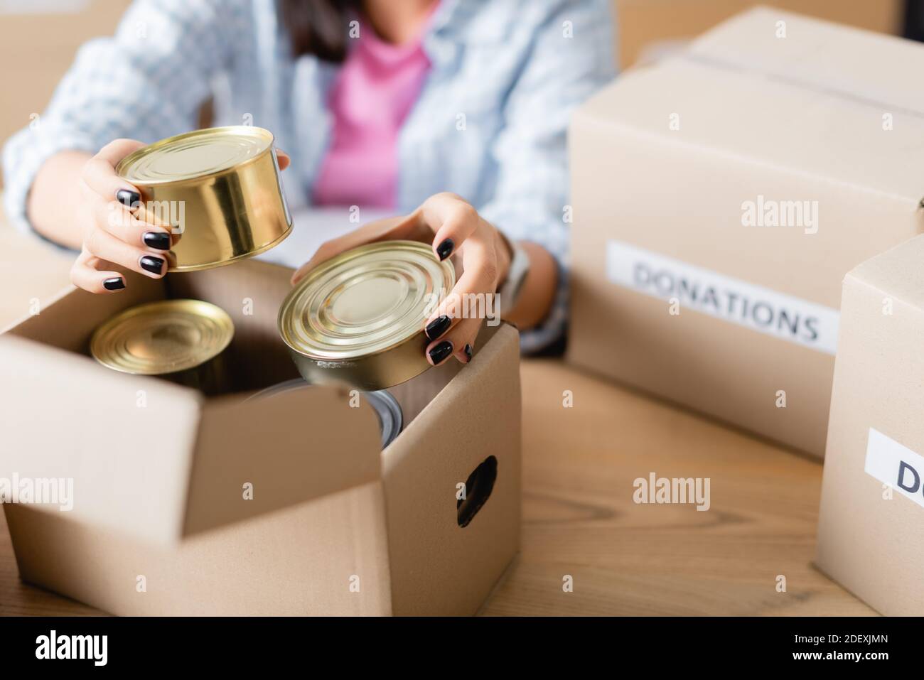 Vue rognée d'une femme tenant des aliments en conserve près de la boîte en carton dans la charité centre sur un fond flou Banque D'Images