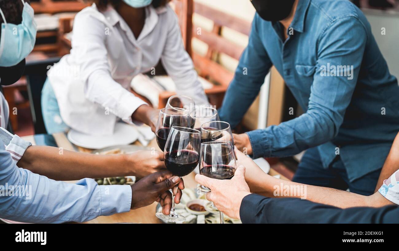 Les jeunes multiraciaux applaudissent avec le vin tout en portant des masques protecteurs - concept de distance sociale - Focus sur la main blanche inférieure Banque D'Images