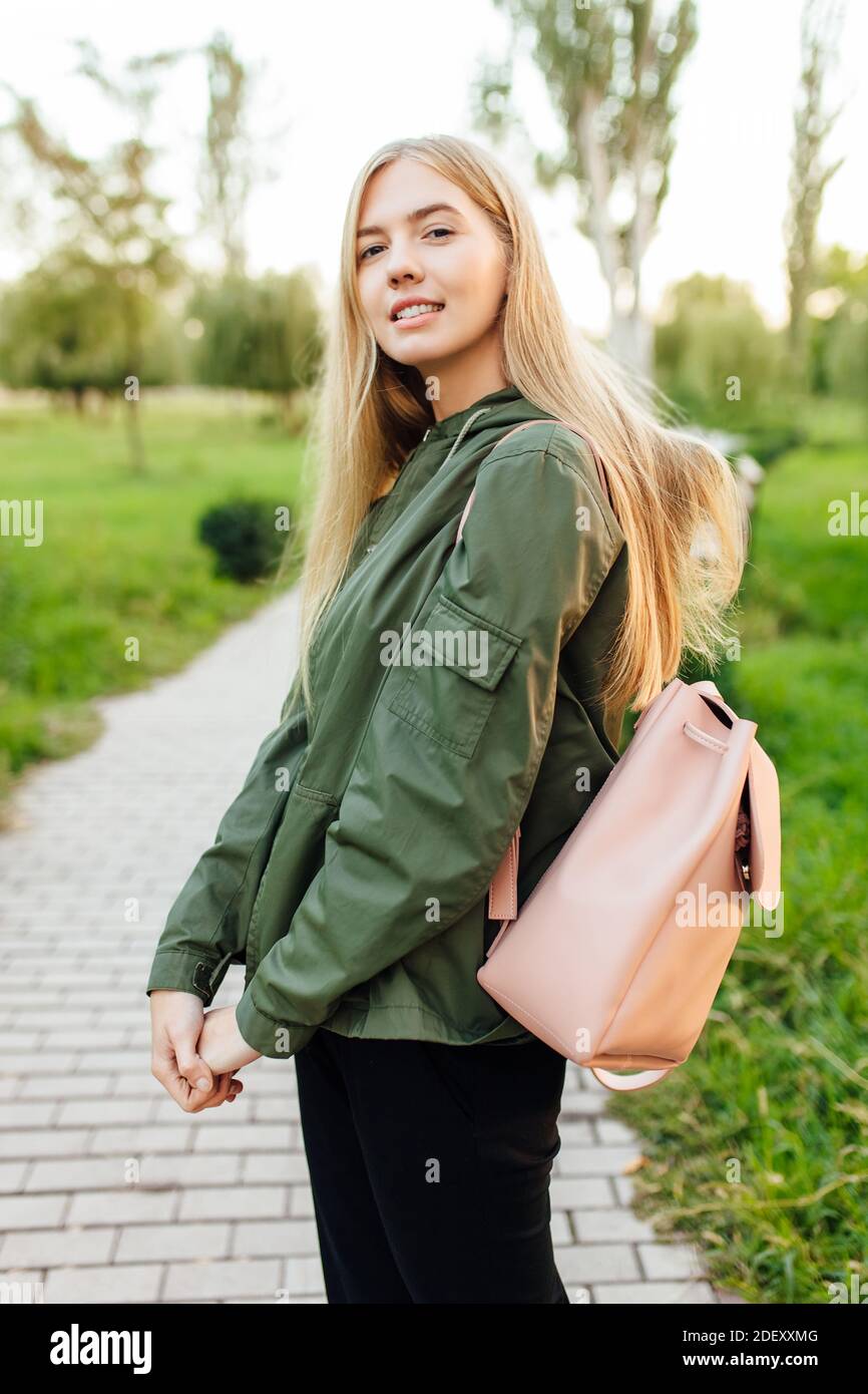 Une belle jeune fille étudiante, vêtue d'une veste avec une serviette, marche dans le parc de bonne humeur Banque D'Images