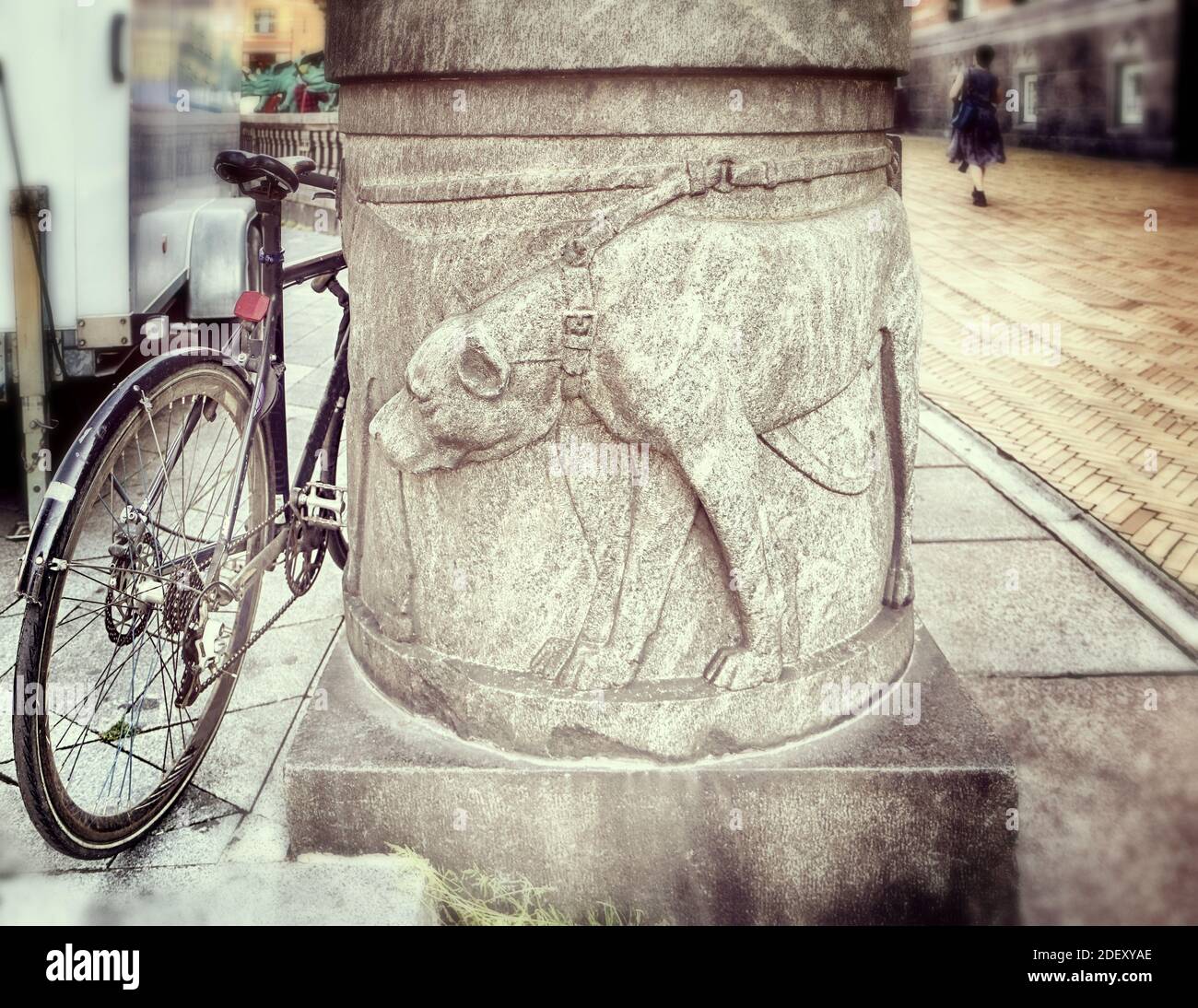 Un chien à collier sculpté à la base d'une colonne le long de la passerelle semble intéressé par une roue à vélo garée à proximité (pour prendre une fuite?), Copenhague Banque D'Images