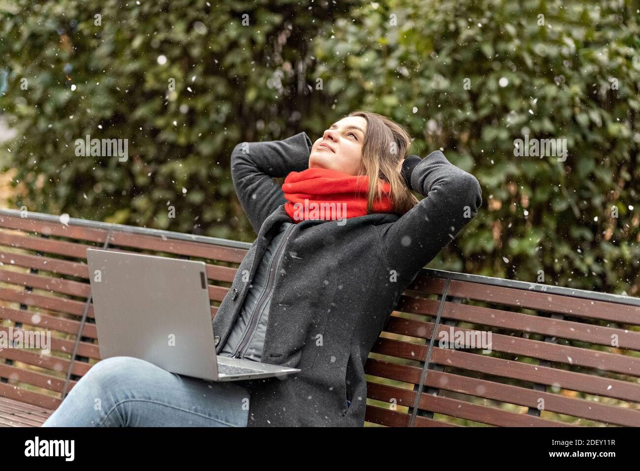 Une jeune femme, avec ses mains derrière sa tête, sent la paix, repose après le travail, est assise sur un banc en bois dans le parc un ordinateur portable sur ses genoux. Pause pendant W Banque D'Images