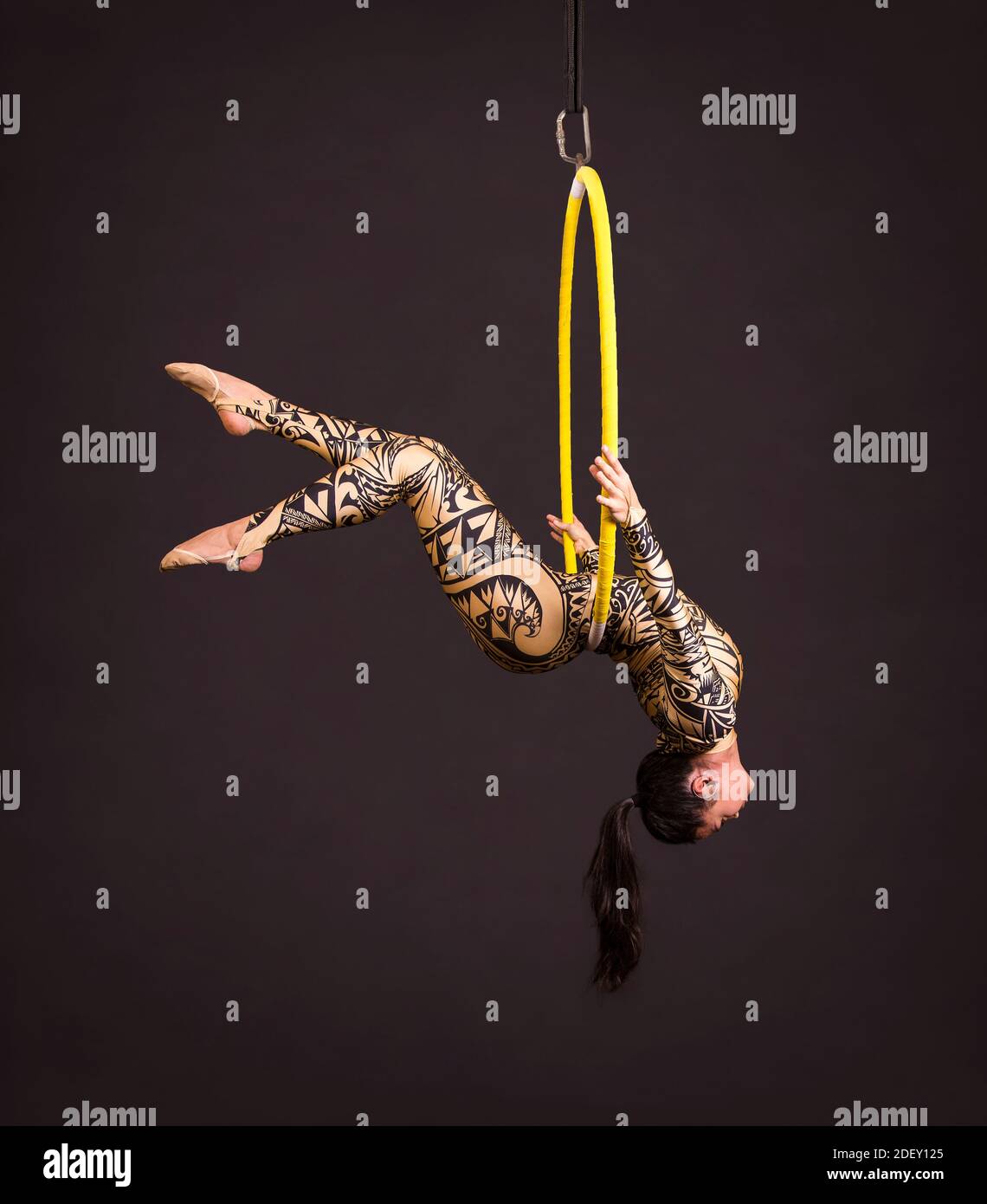 Une jeune femme en costume avec un imprimé présente des éléments acrobatiques dans l'anneau d'air. Des performances en studio sur fond noir. Banque D'Images