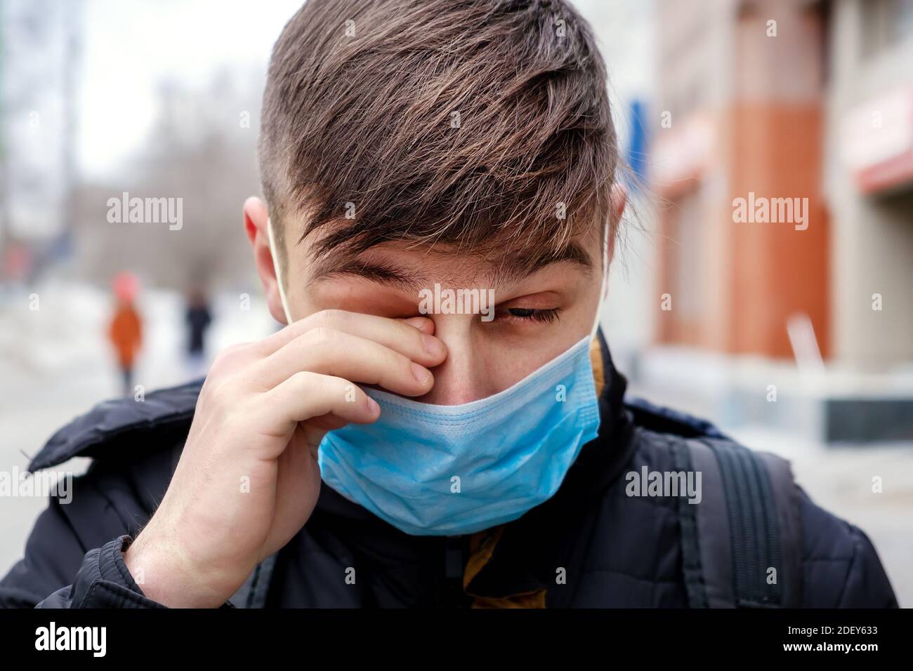 Jeune homme dans le masque de la grippe sur la rue de la ville Frottez son œil Banque D'Images