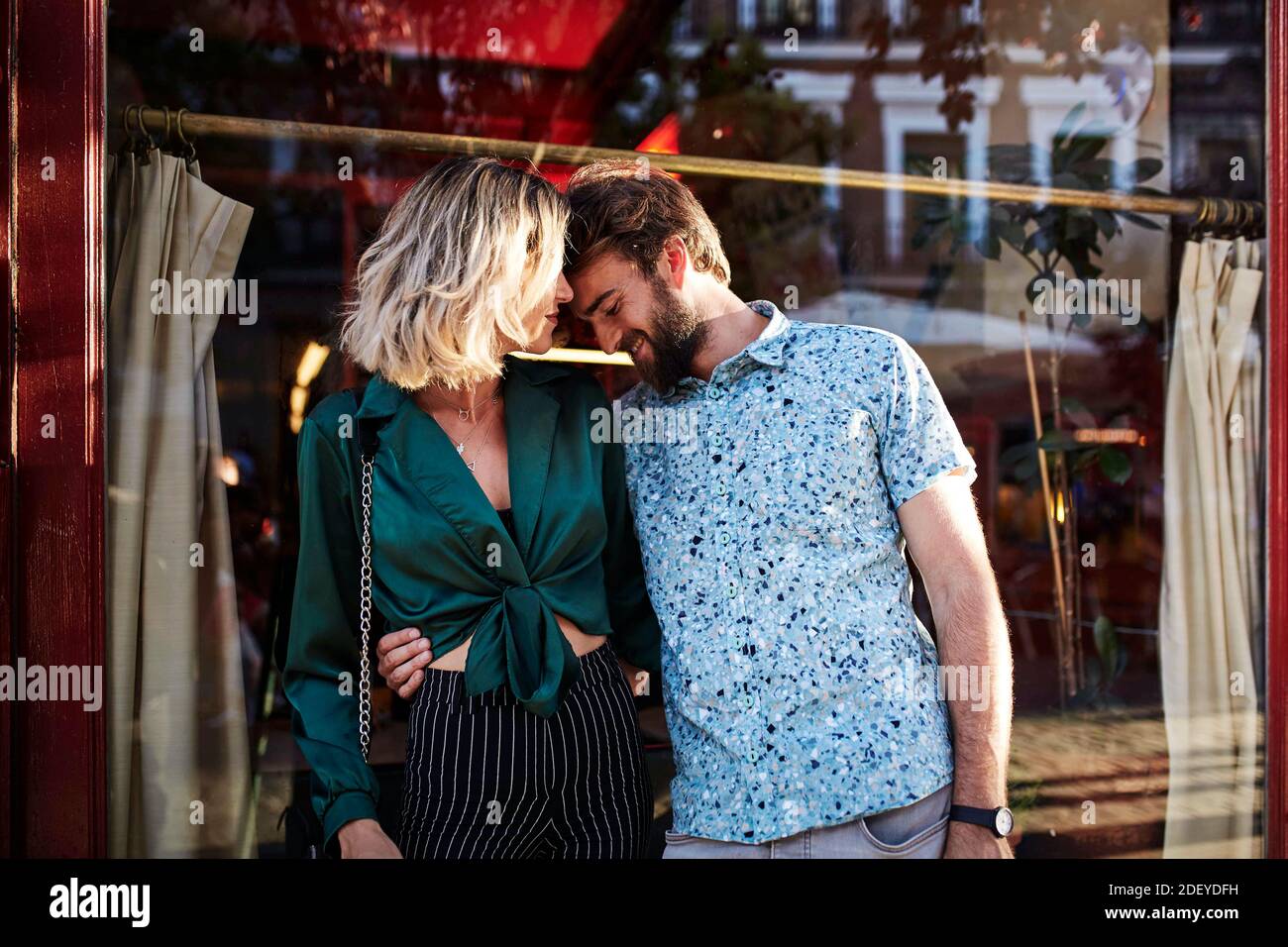 Photo d'un couple dans leur 30s debout dans la rue. L'homme a ses mains autour de la femme et sa tête sur son épaule. Ils portent le cas Banque D'Images