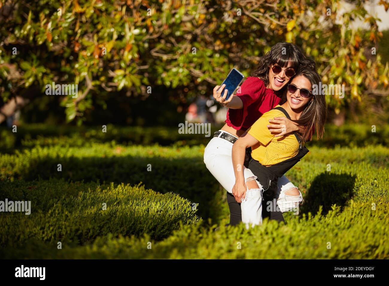 Photo de deux adolescentes prenant un selfie. L'un d'eux est sur les autres dos. Ils portent un tissu décontracté et des lunettes de soleil. Banque D'Images