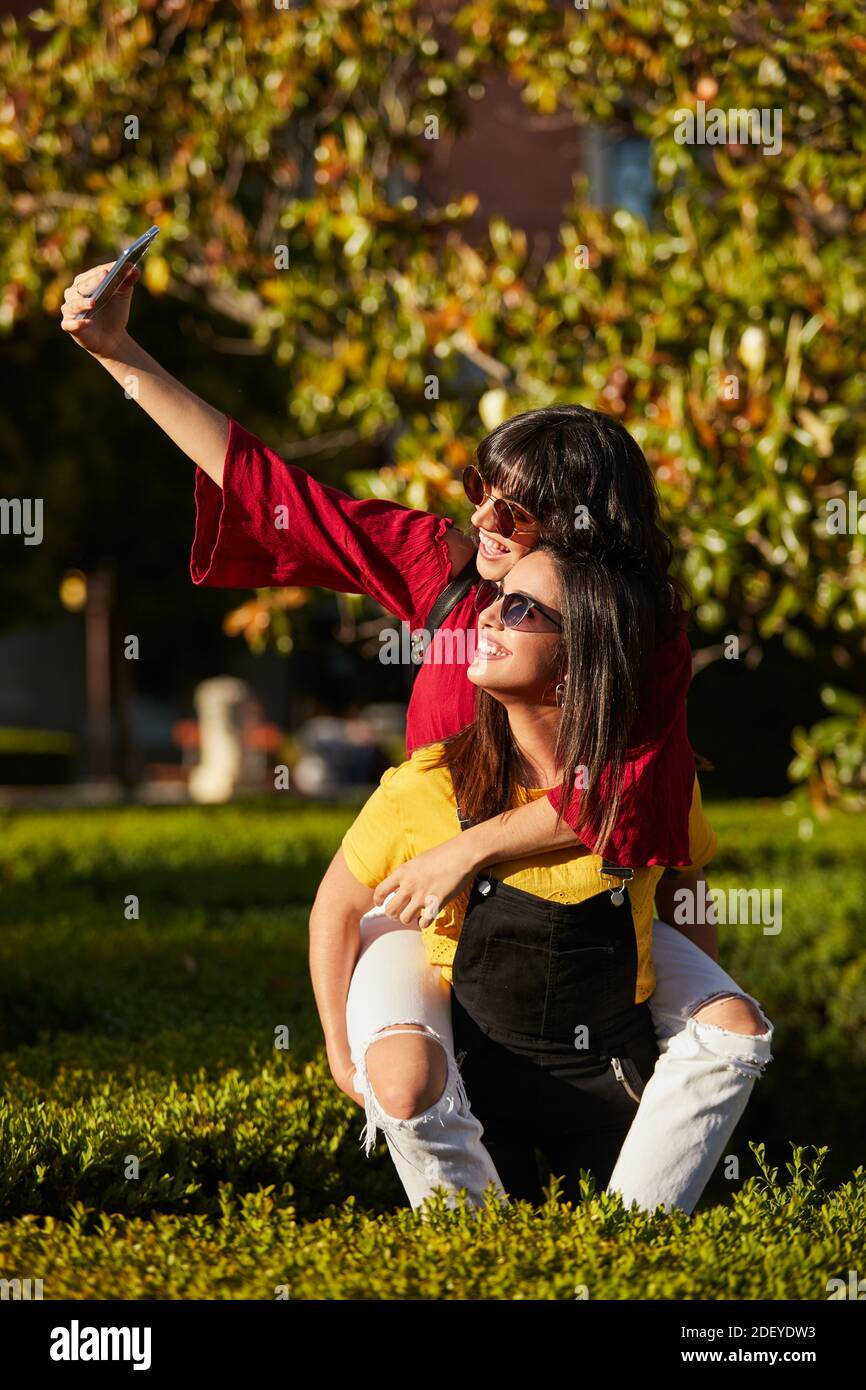 Photo de deux adolescentes prenant un selfie. L'un d'eux est sur les autres dos. Ils portent un tissu décontracté et des lunettes de soleil. Banque D'Images