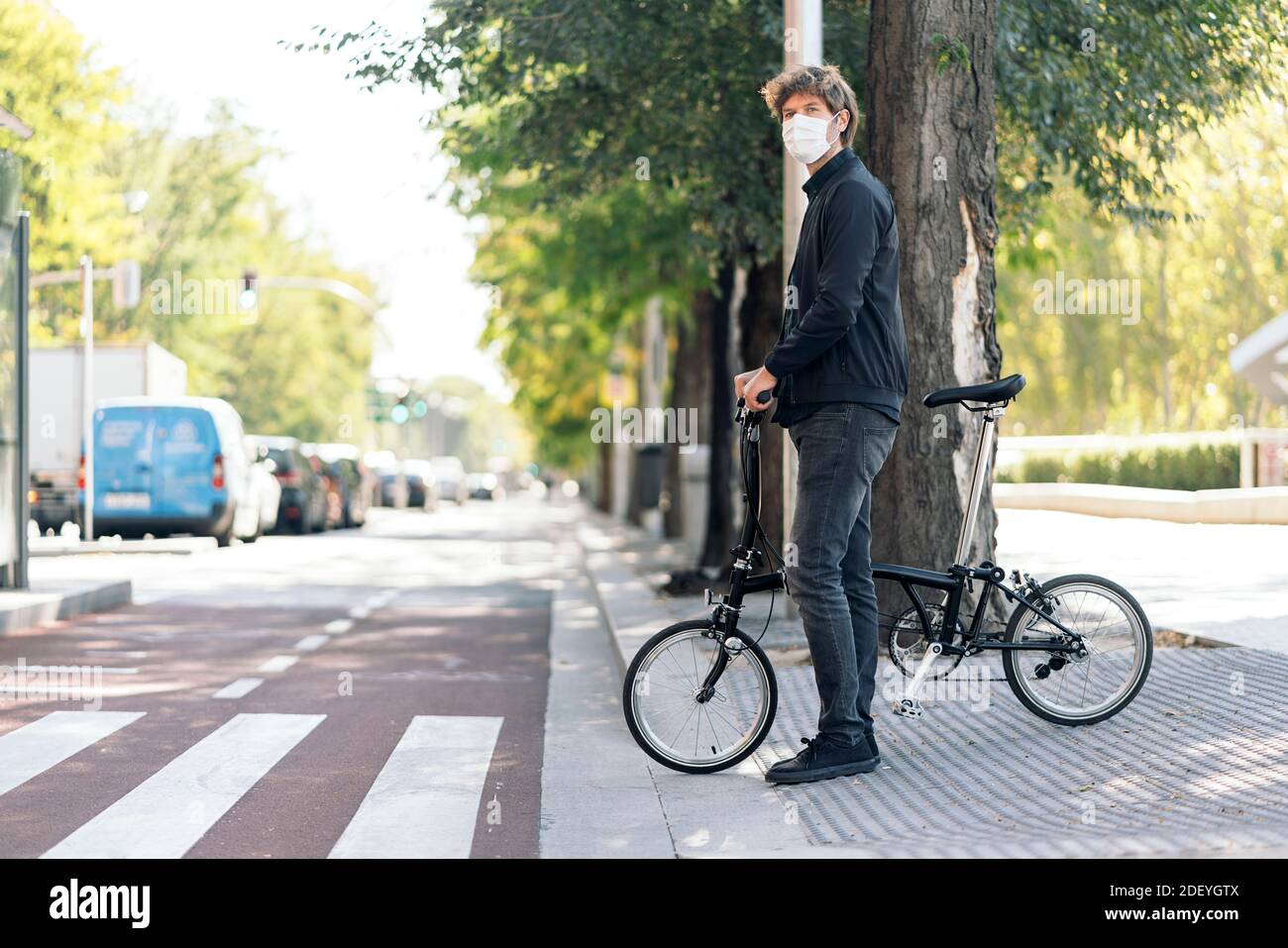 Photo de l'homme beau portant un masque facial avec son vélo amovible dans la rue. Banque D'Images