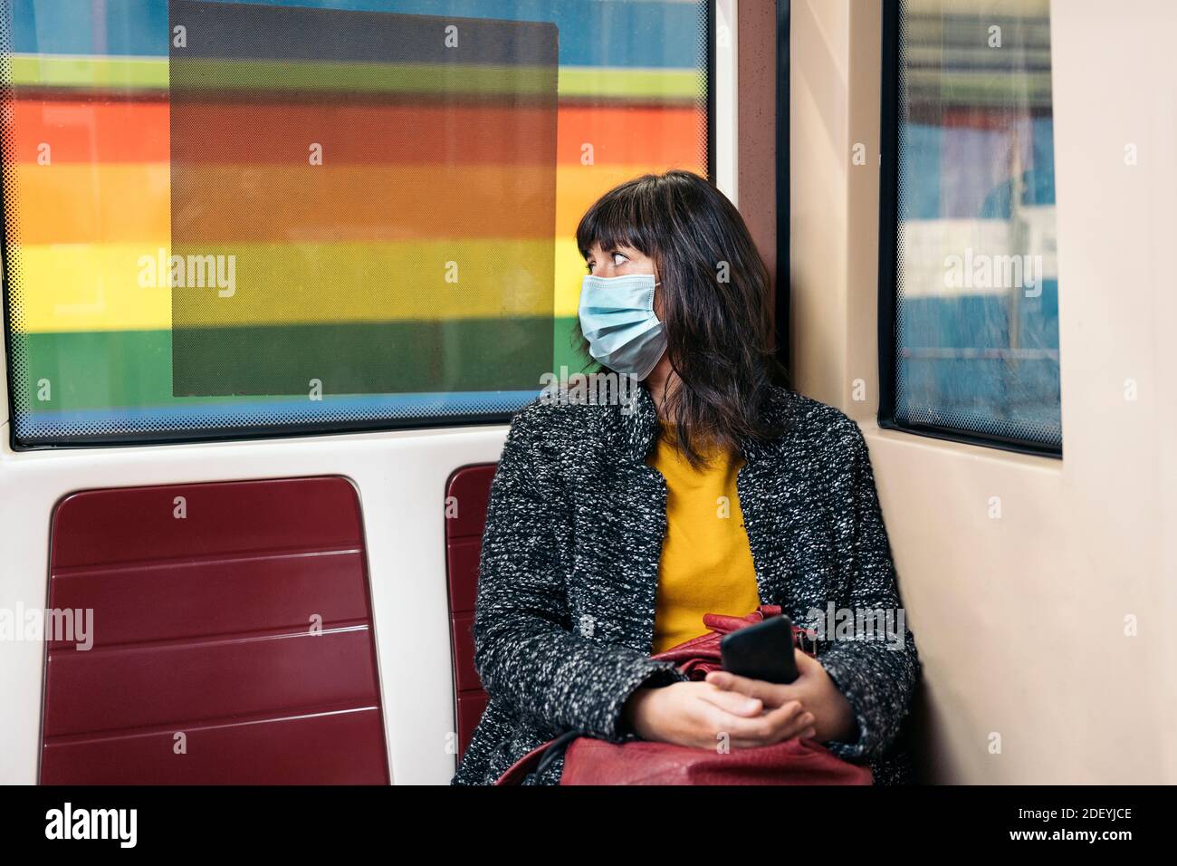 Photo de la femme élégante portant un masque de visage en raison de covid19 assis à l'intérieur d'un wagon de métro regardant par la fenêtre. Banque D'Images