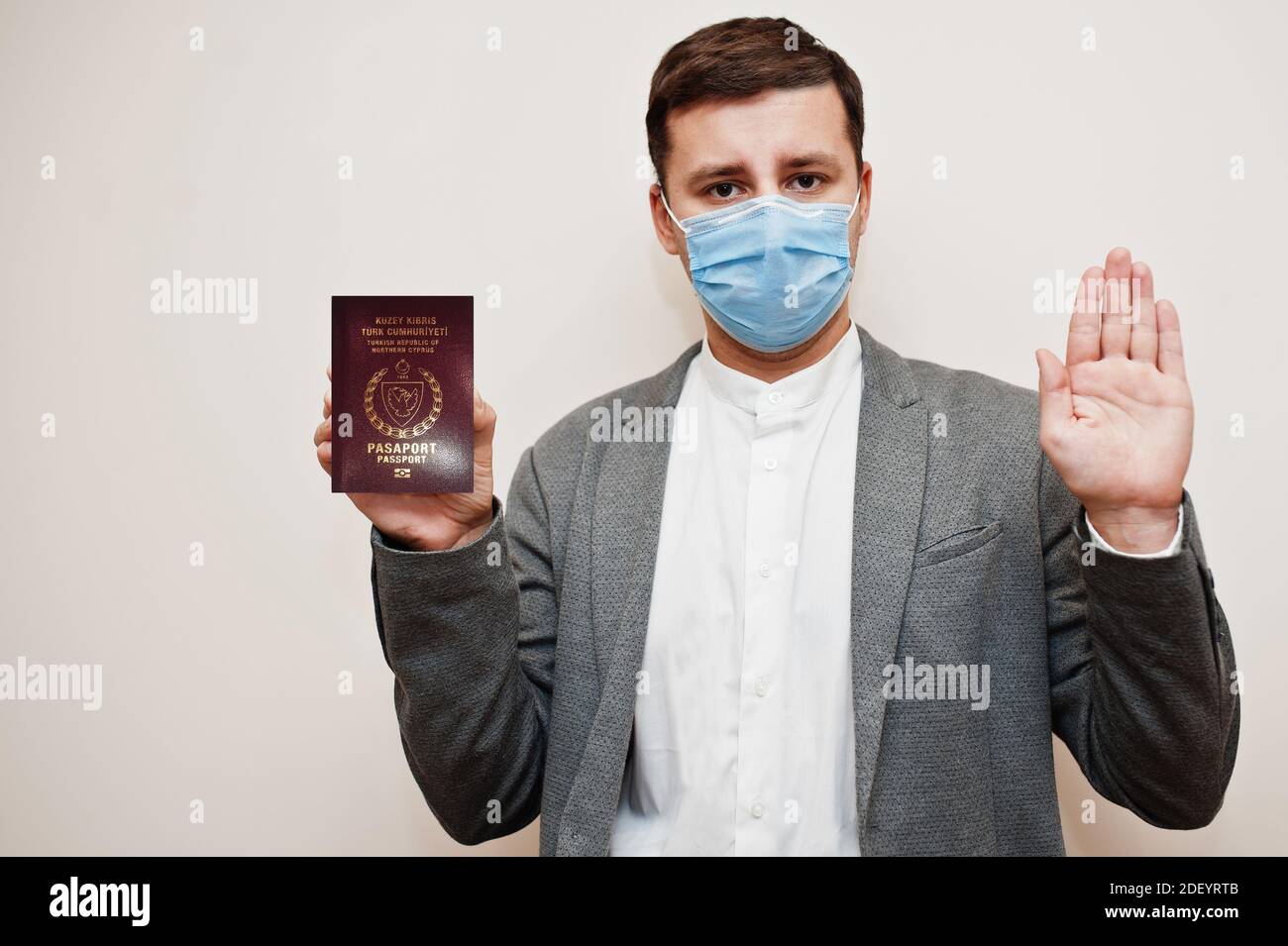 Homme européen en tenue officielle et masque facial, montrez le passeport de Chypre du Nord avec le panneau stop main. Confinement du coronavirus en Europe concept de pays. Banque D'Images