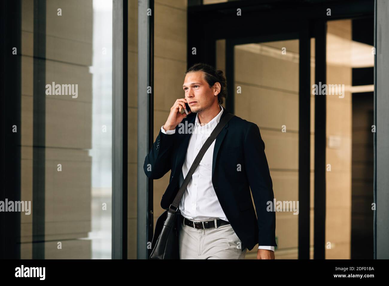 Homme d'affaires confiant parlant sur un smartphone tout en sortant d'un bâtiment de bureau Banque D'Images