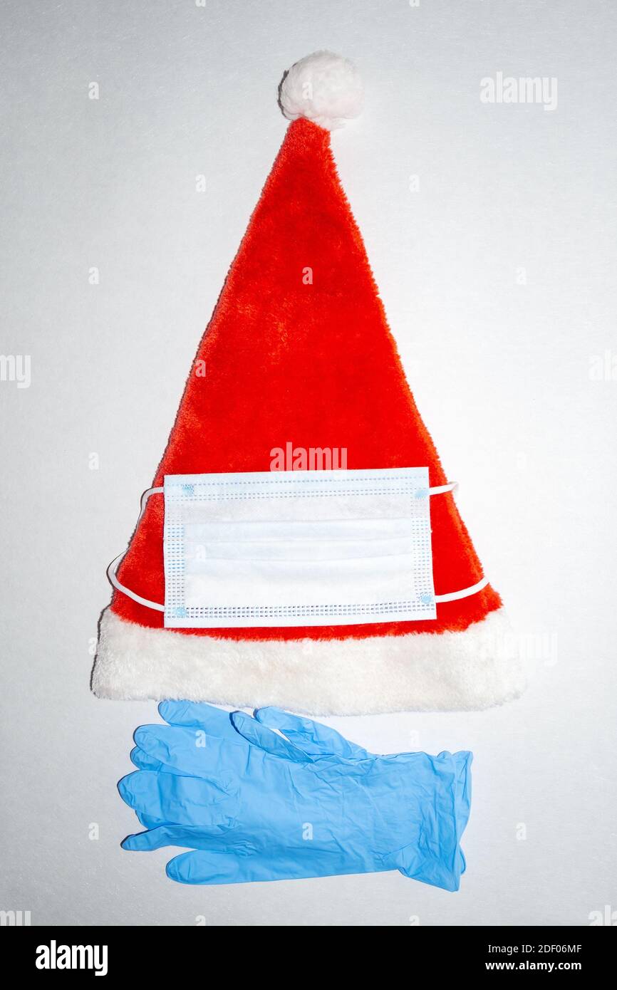 Chapeau de Noël en peluche rouge et blanc avec masque chirurgical et une paire de gants en vinyle médical bleus. Vue verticale du dessus Banque D'Images