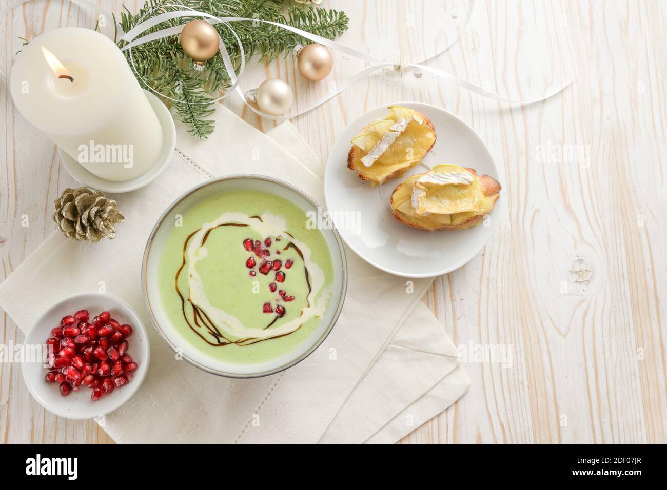 Soupe de crème de fête à base de pommes et de petits pois avec graines de grenade et baguette de camembert cuite au four, apéritif pour un repas de vacances sur une table en bois blanc avec Banque D'Images