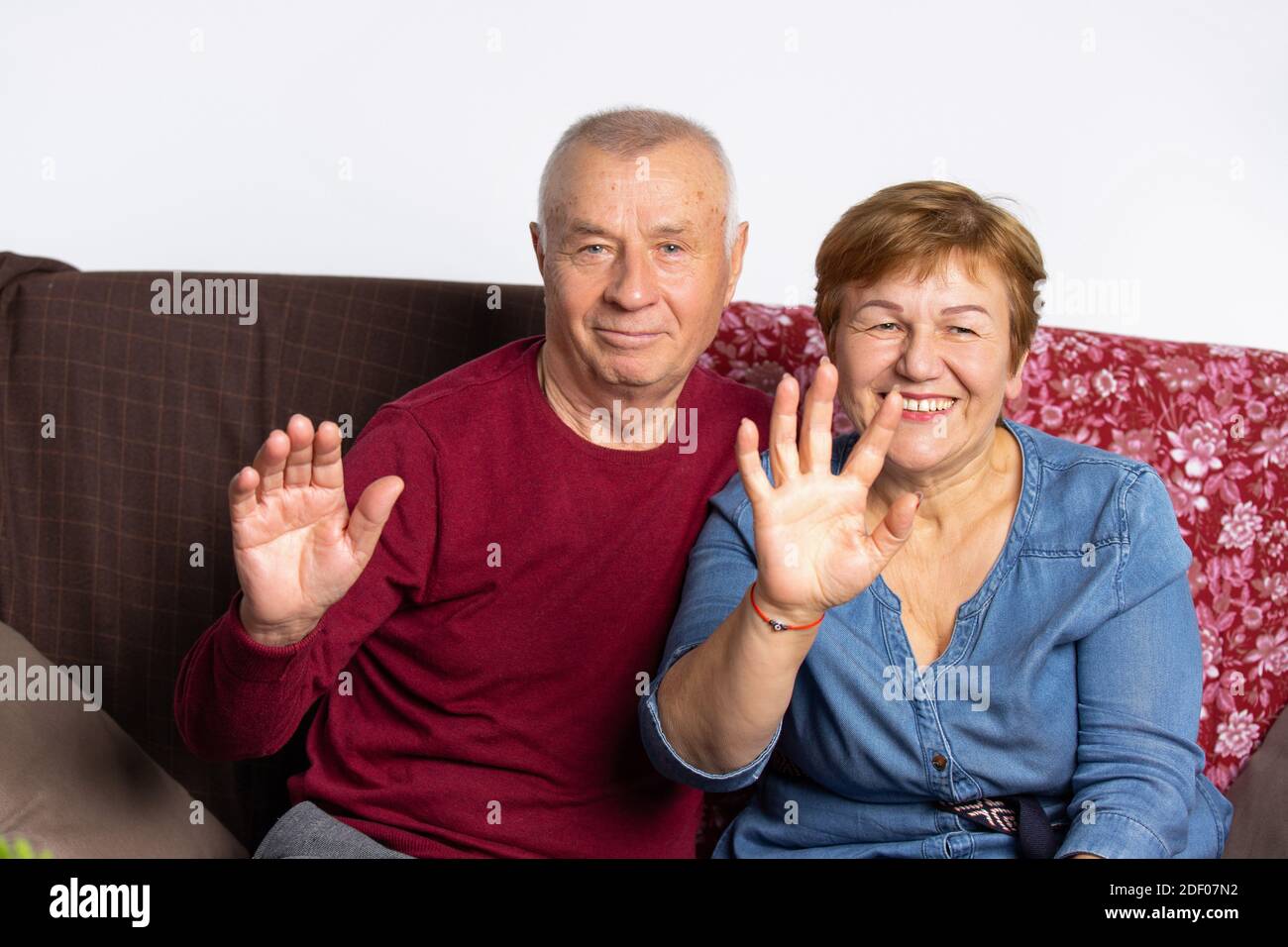Portrait d'un couple âgé assis sur le canapé et en agitant les mains devant la caméra. Banque D'Images