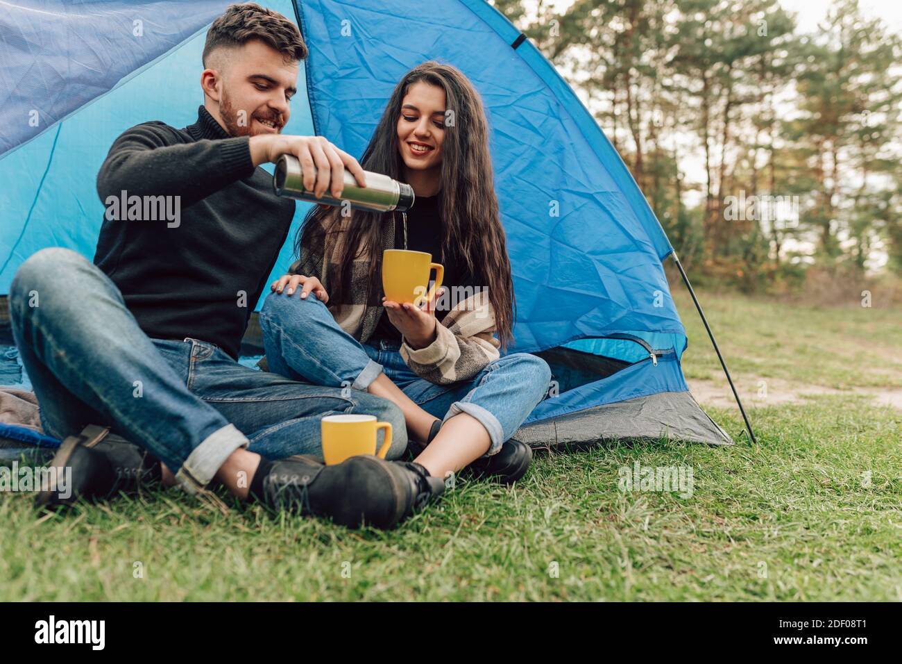 Le bonheur couple dans la nature avec tente, boisson chaude. L'homme verse du thé du thermos à sa femme Banque D'Images