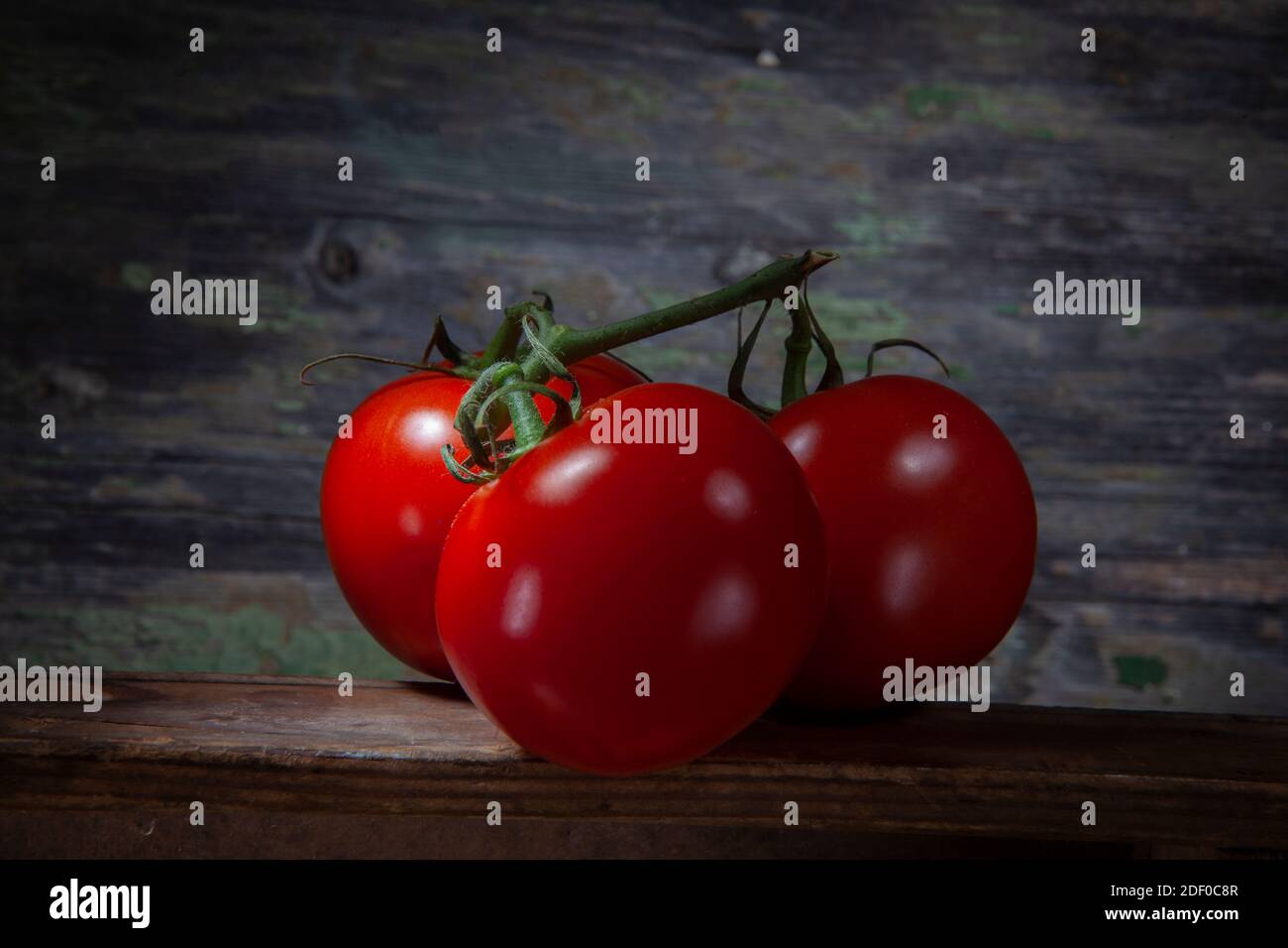 Prise de vue macro de trois tomates rouges fines et vives sur la table Et fond en bois décalé Banque D'Images