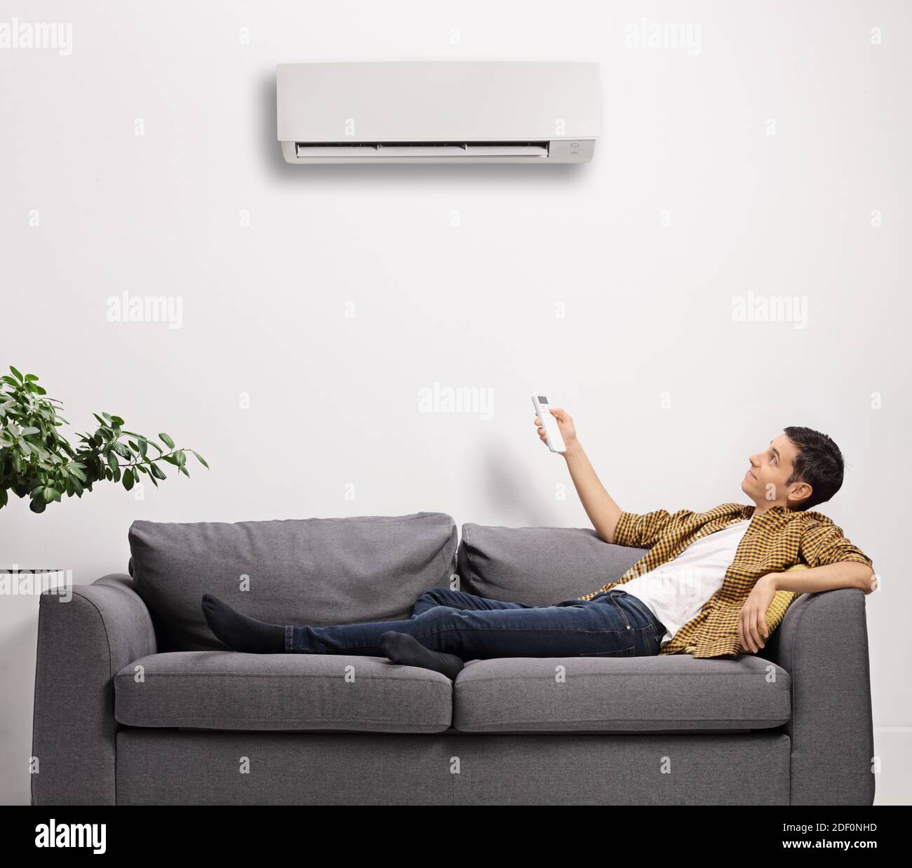 Jeune homme allongé sur un canapé avec une télécommande réglage de l'unité de climatisation isolée sur fond blanc Banque D'Images