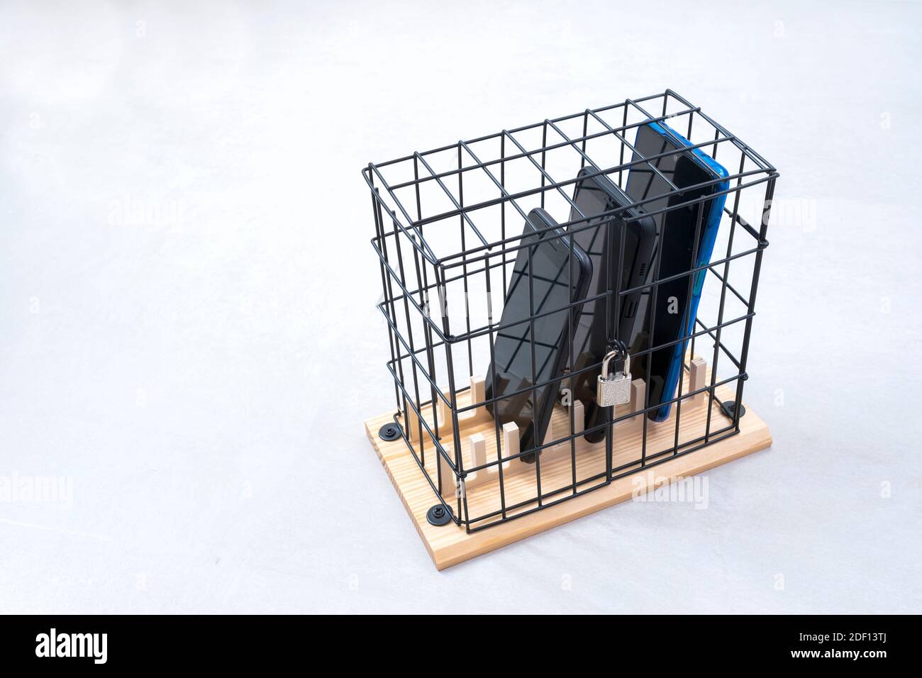 trois téléphones portables enfermés dans une cage avec un cadenas, concept d'isolement social ou d'abus de téléphone et de réseaux sociaux, fond blanc horizontal Banque D'Images