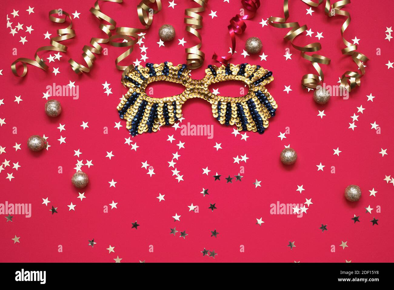 Masque étincelant doré, serpentine et étoiles dorées avec ornements de Noël sur fond rouge. Vue de dessus, espace de copie. Concept de célébration du Carnaval Banque D'Images
